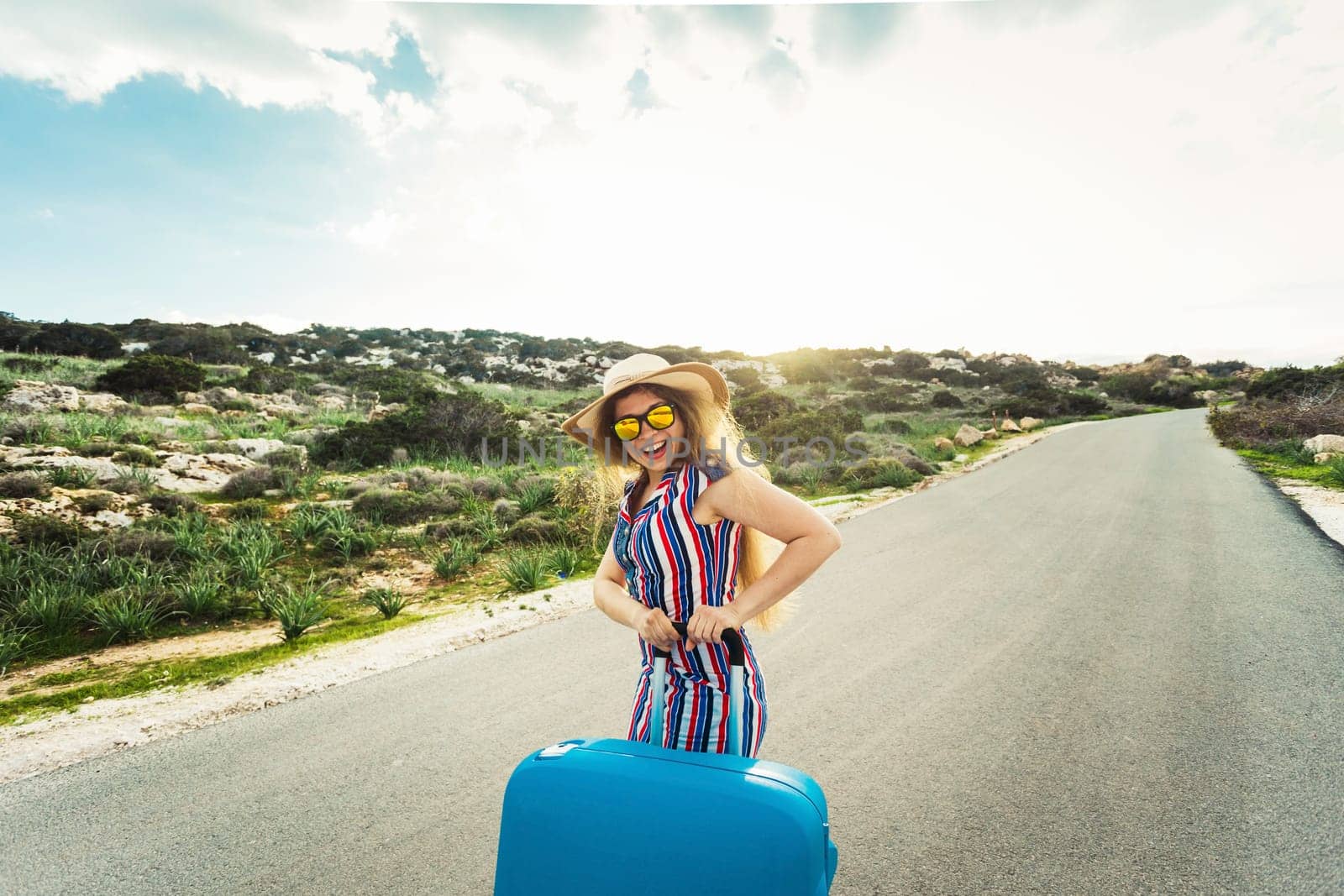Travel, holiday, summer and vacation concept - Young woman is standing and laughing on road with suitcases.
