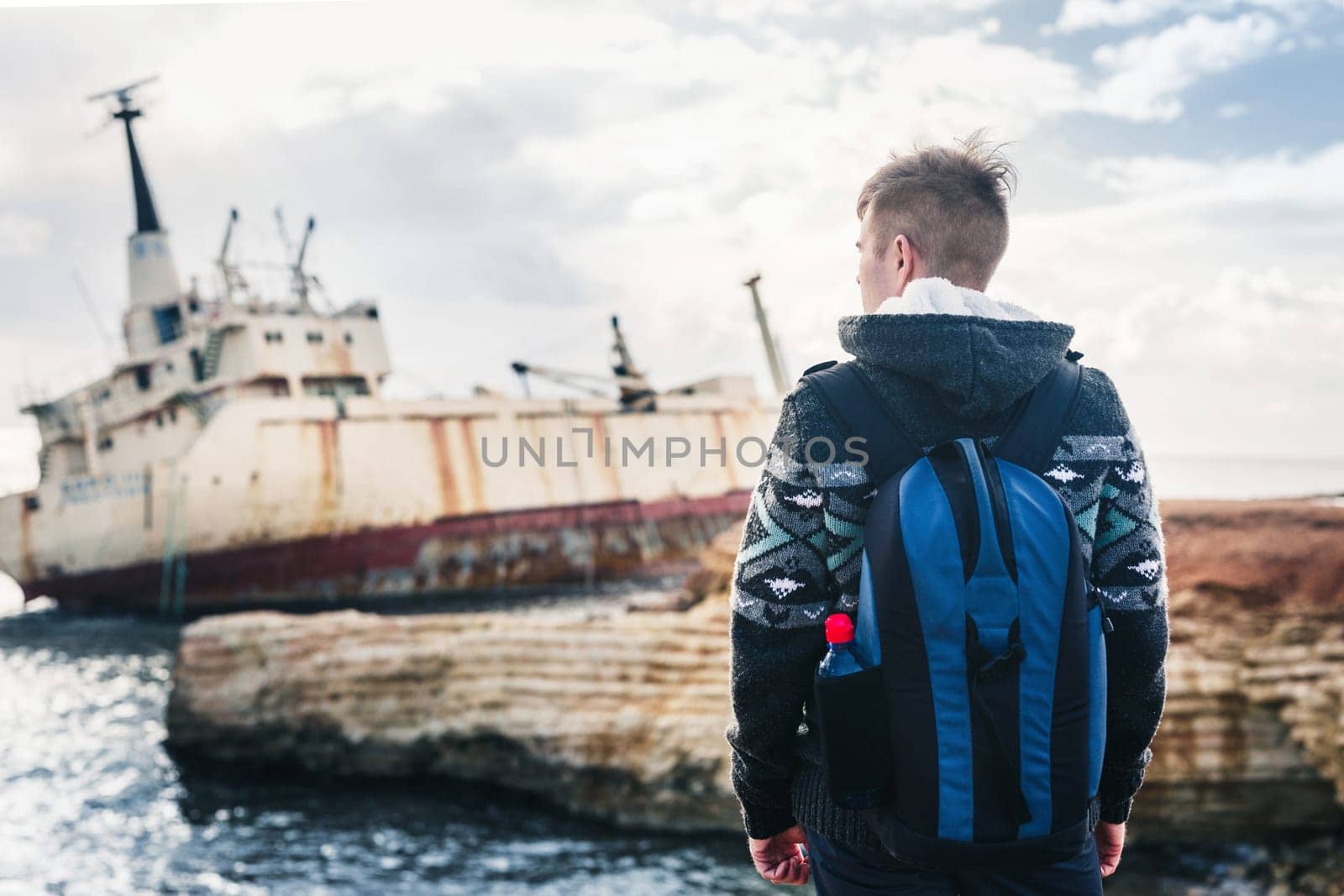 Male tourist looking at an abandoned ship on the sea or ocean. Adventure and tourism concept