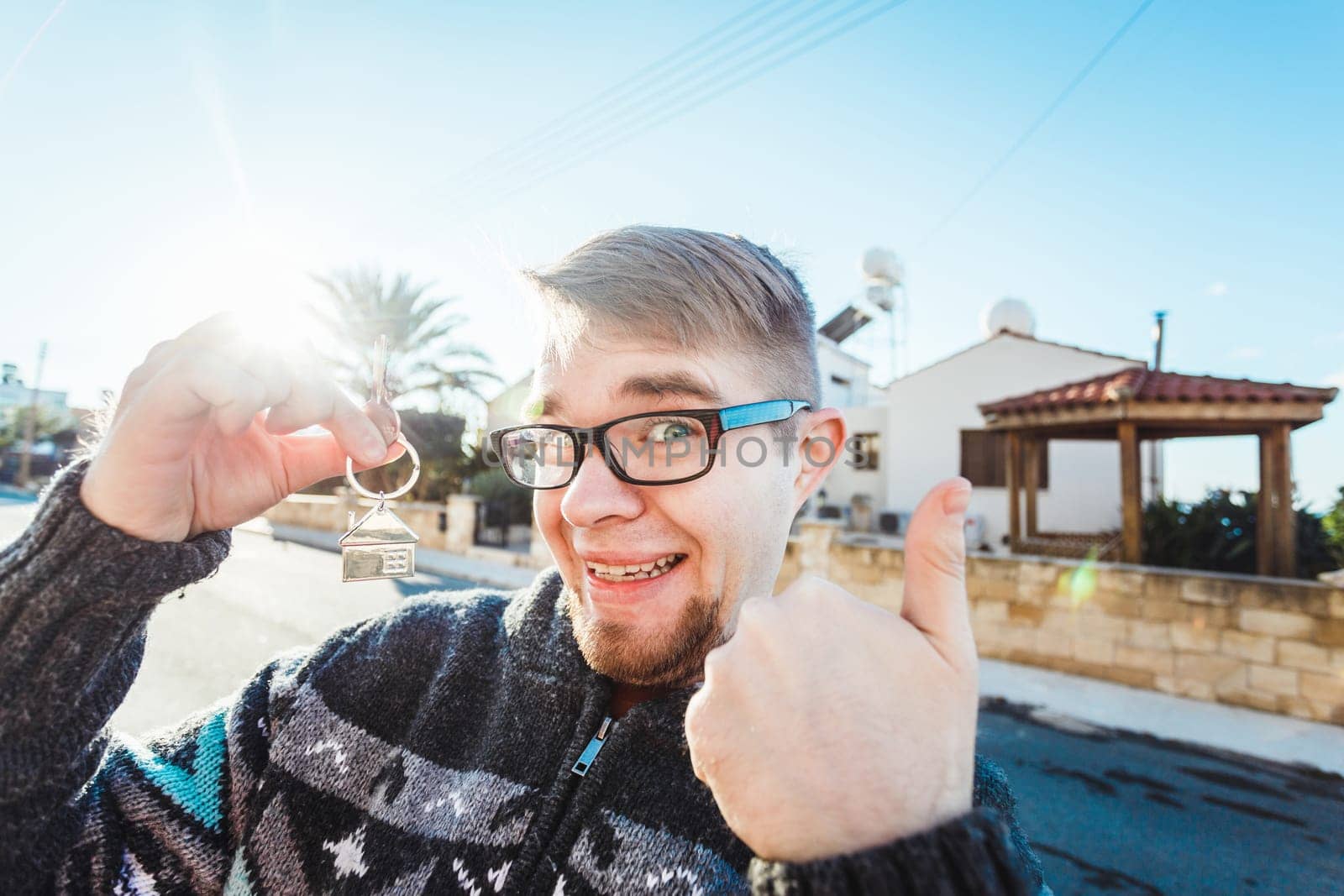 Portrait of a young man holding out new house key while gesturing thumbs up