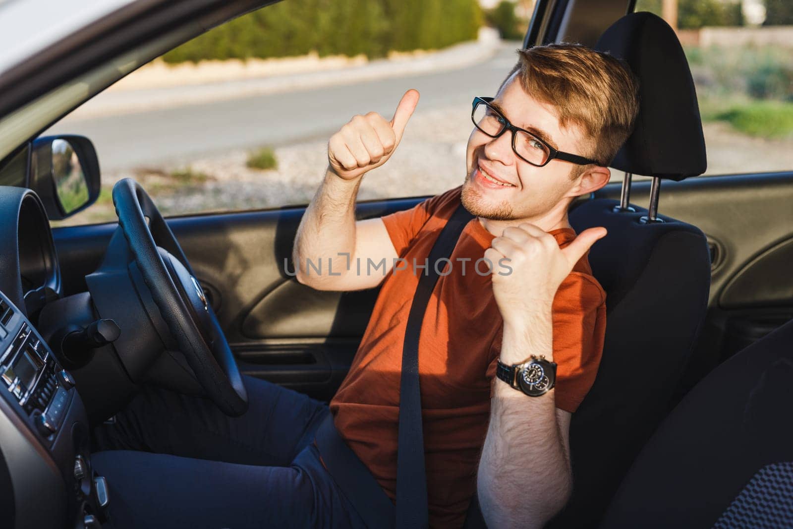Young man smiling and showing thumbs up in his car.