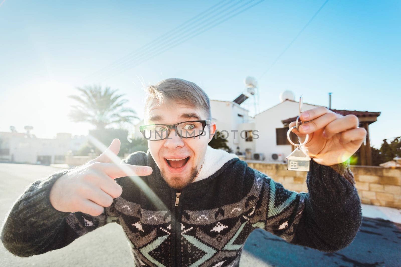 Joyful man shows keys on the background of new home.