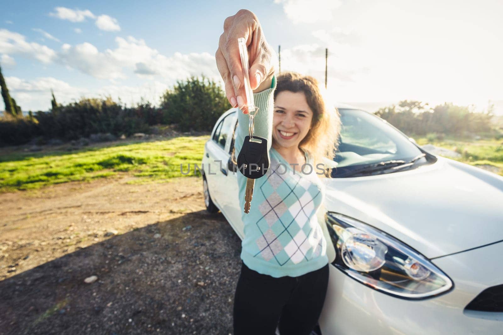 Young woman holding keys to new car and smiling at camera.