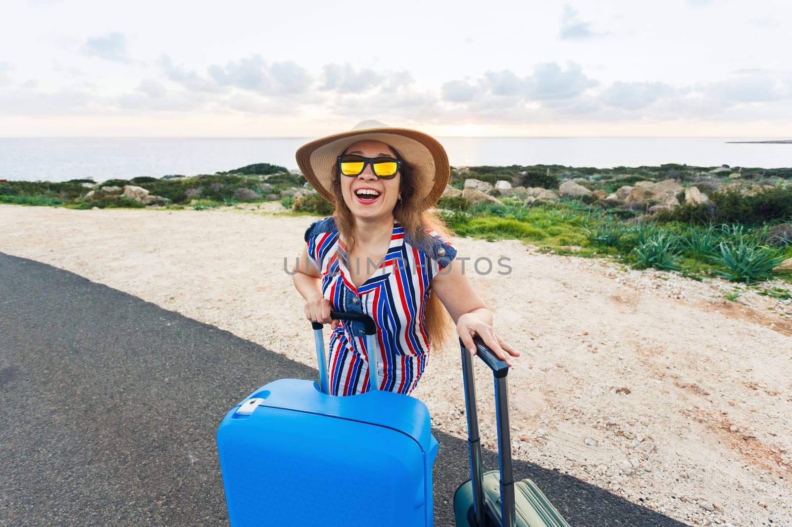 Travel, holiday, summer and vacation concept - Young woman is standing and laughing on road with suitcases.