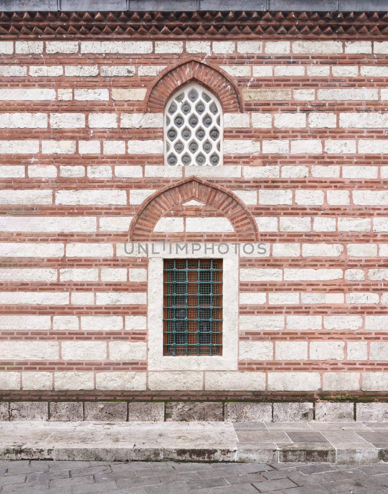 External wall of 16th century Selman Aga Mosque in Uskudar, Istanbul, Turkey. The wall is made of red brick and has arched perforated stucco and wrought iron windows