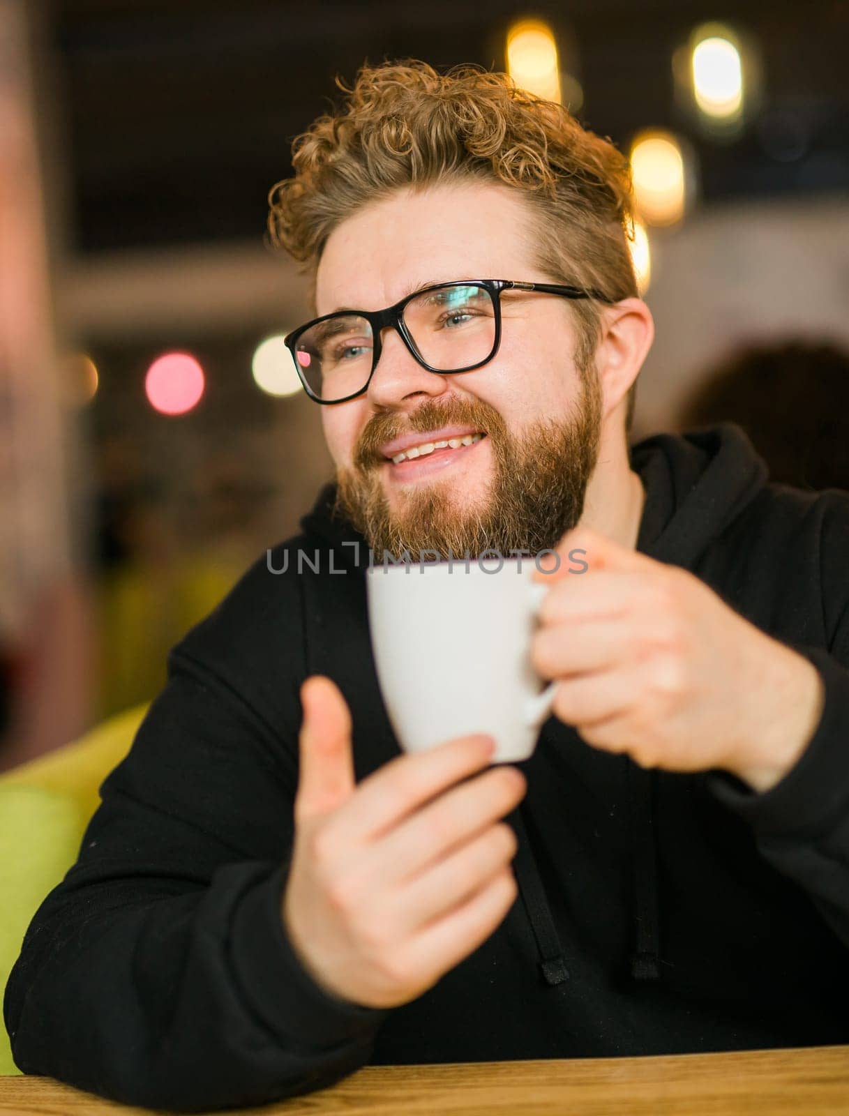 Bearded curly man smiling confident drinking coffee in restaurant or coffee shop. Millennial generation and Gen Y.