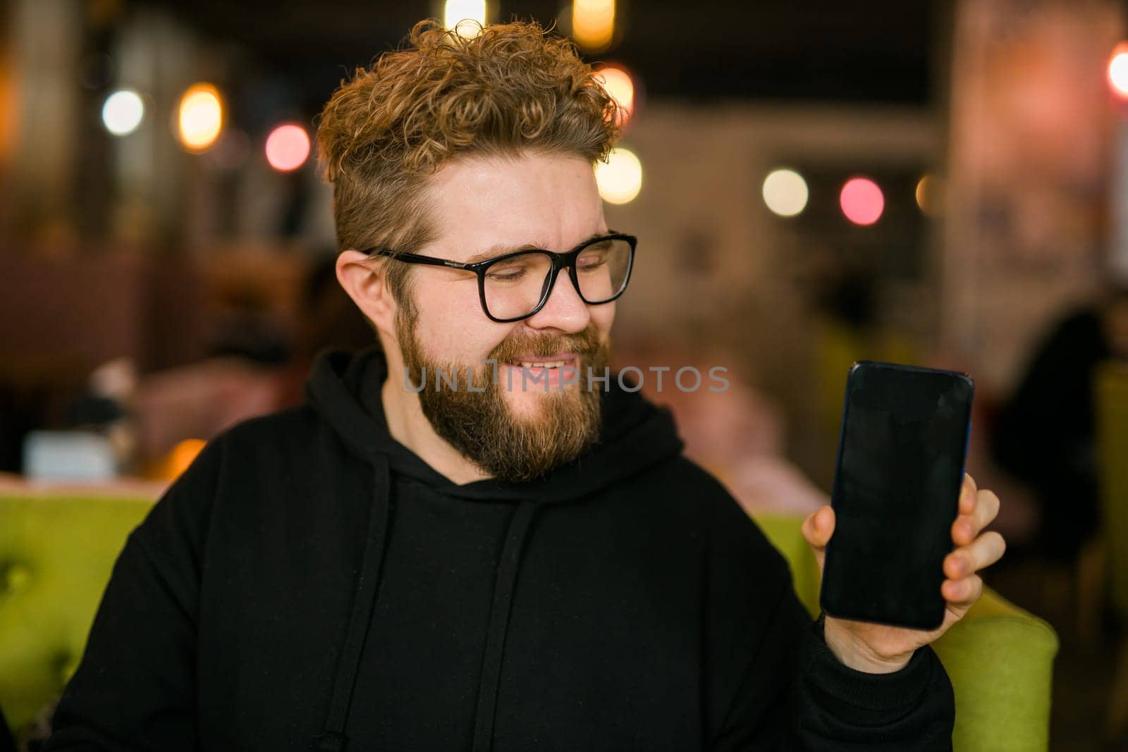 Satisfied man with dark beard holding smartphone and showing his favorite mobile app Male programmer has developed a cool application