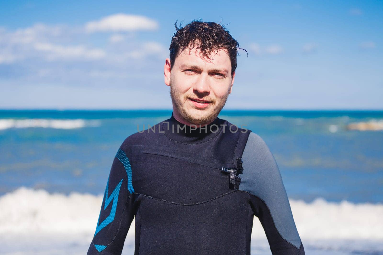 Male surfer beach lifestyle portrait. Man in wetsuit near sea or ocean.