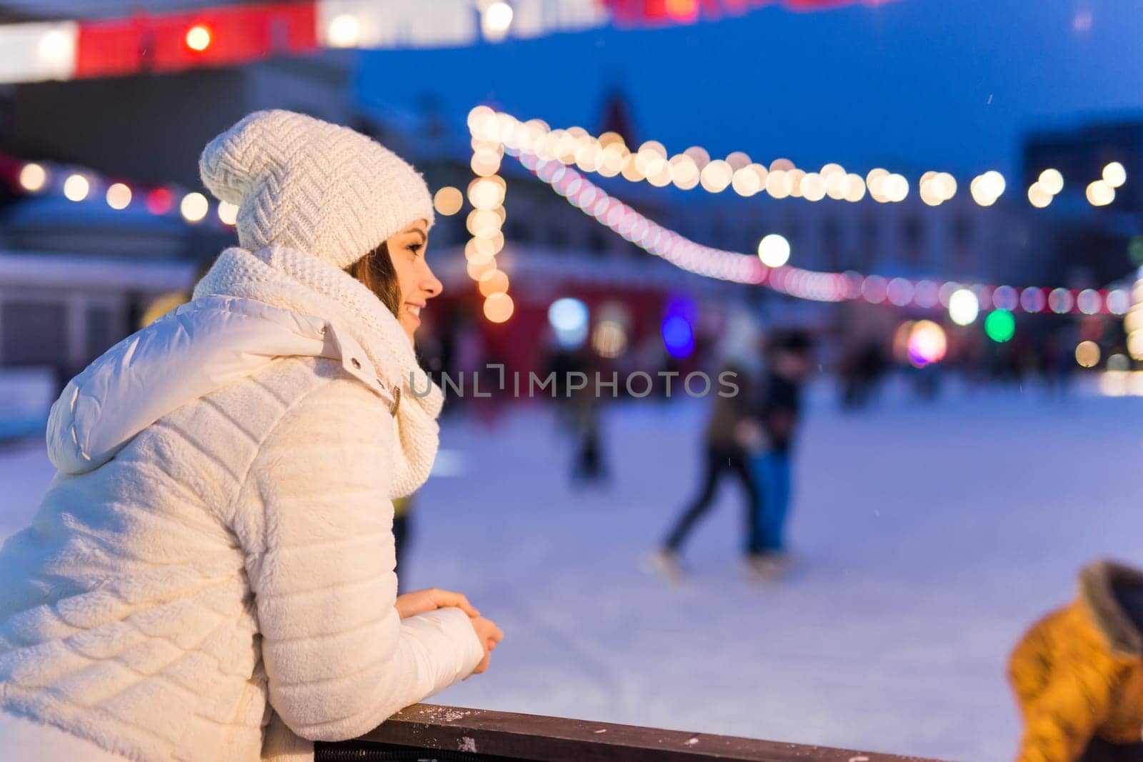 A woman on the rink is skating and taking selfie on smartphone. New Years Eve and Christmas. Fairy lights. Ice and snow mood concept. Winter