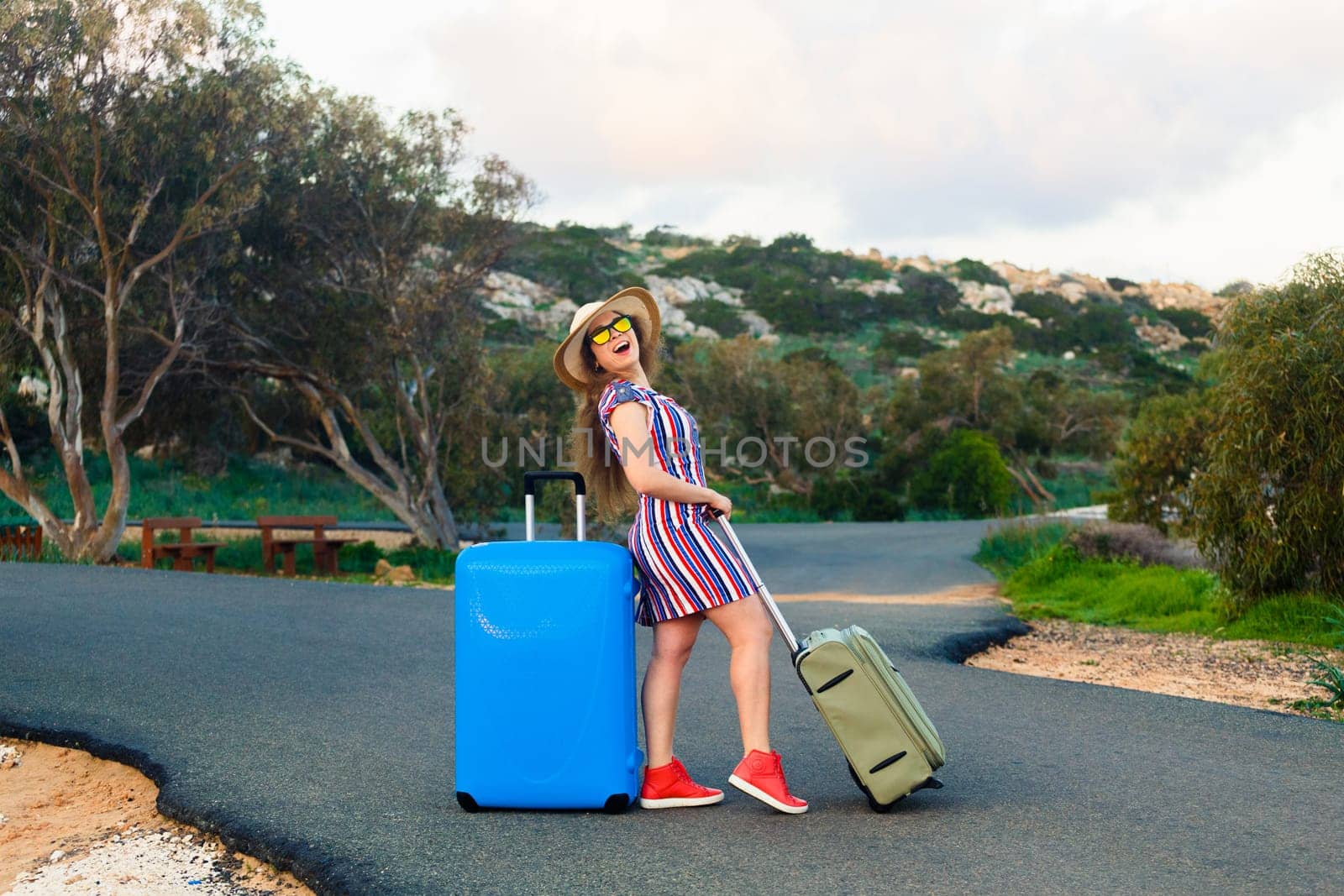 Happy laughing young woman with suitcases on the road