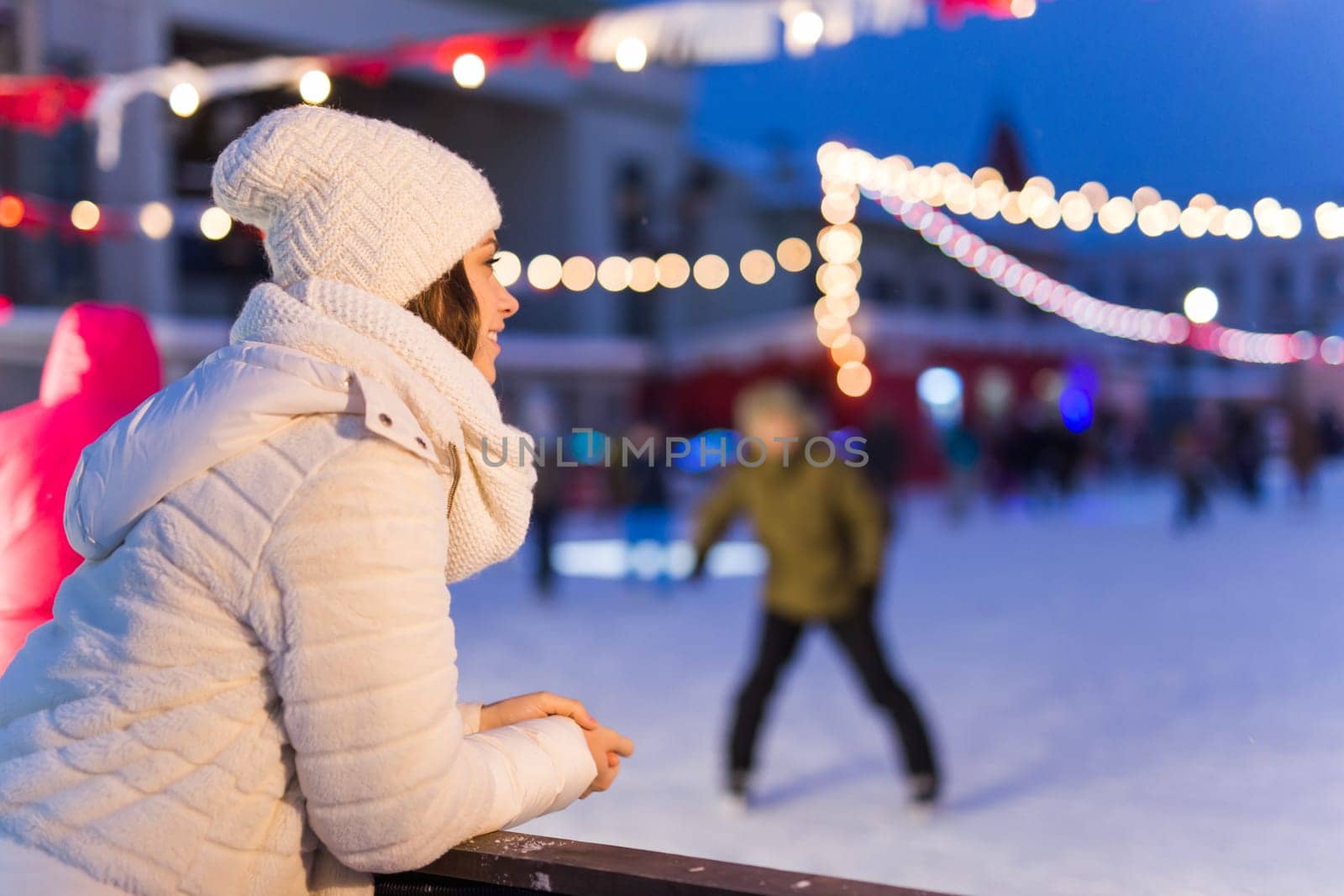 Christmas, winter, technology and leisure concept - happy young woman taking picture with smartphone on ice skating rink.
