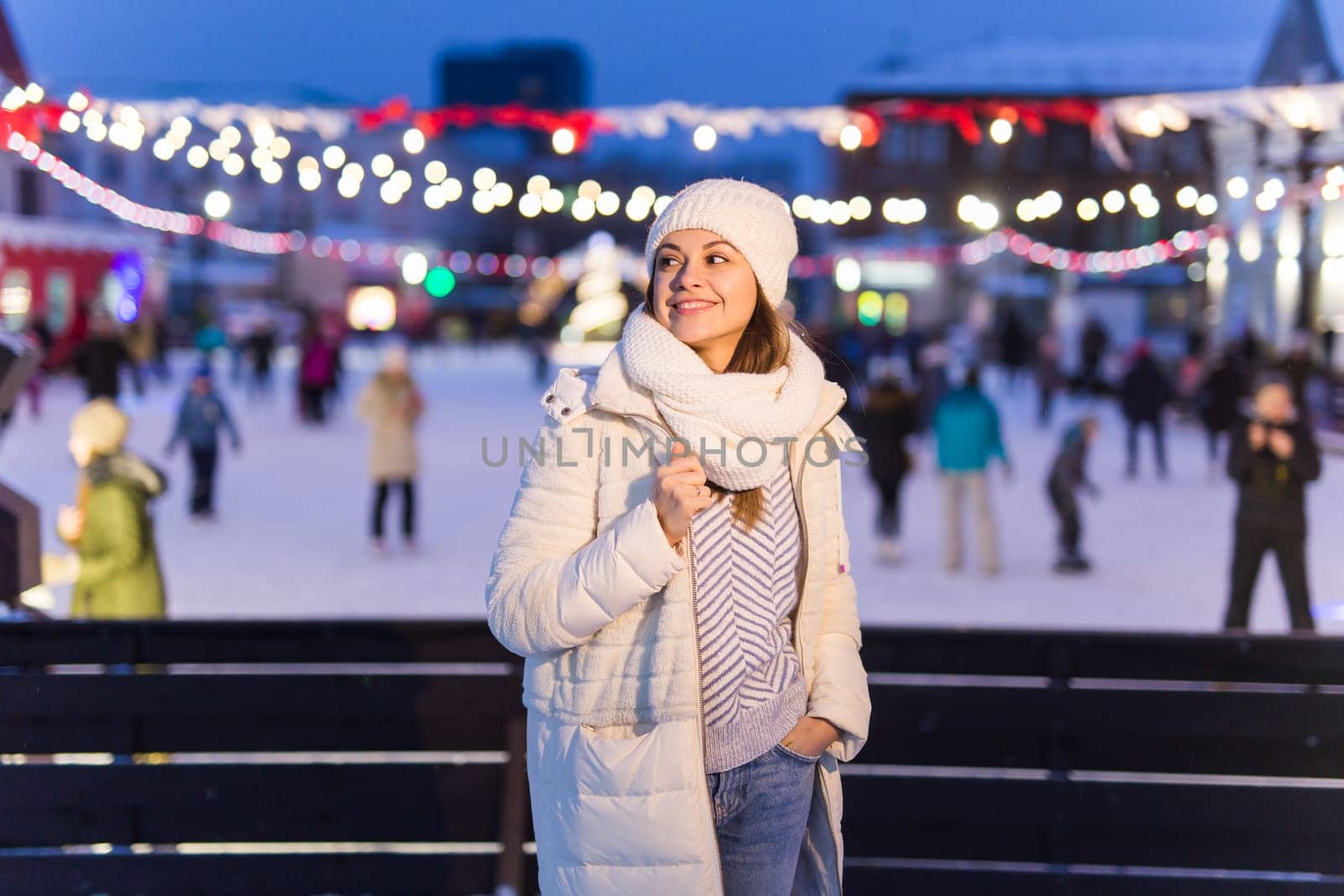 Christmas, winter, technology and leisure concept - happy young woman taking picture with smartphone on ice skating rink.