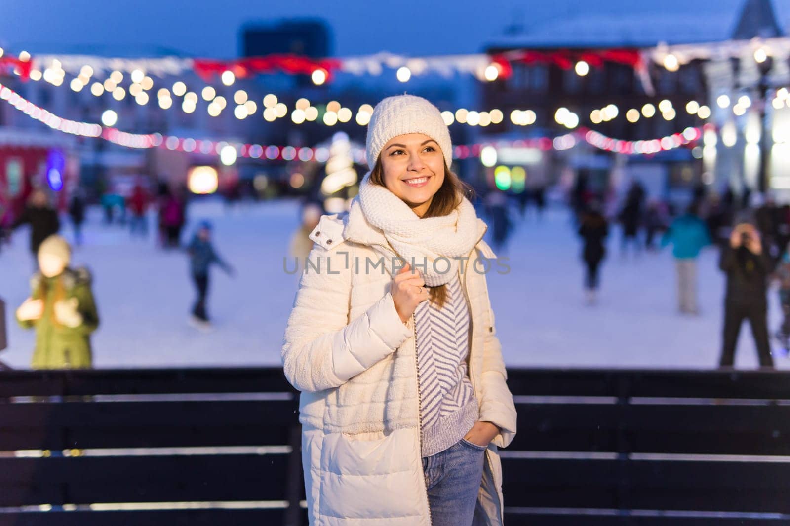 A woman on the rink is skating and taking selfie on smartphone. New Years Eve and Christmas. Fairy lights. Ice and snow mood concept. Winter