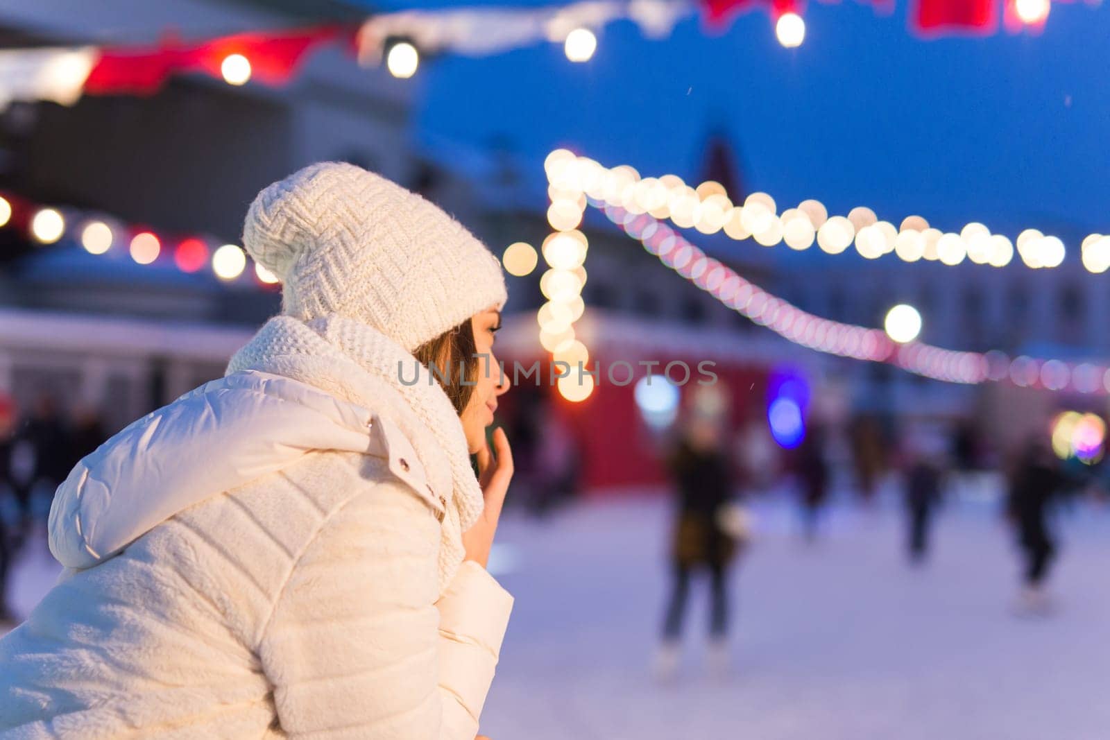 Christmas, winter, technology and leisure concept - happy young woman taking picture with smartphone on ice skating rink.