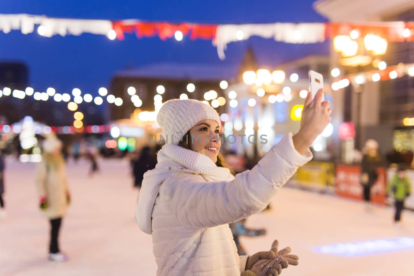 Happy young woman in winter on the ice rink taking picture on smartphone.