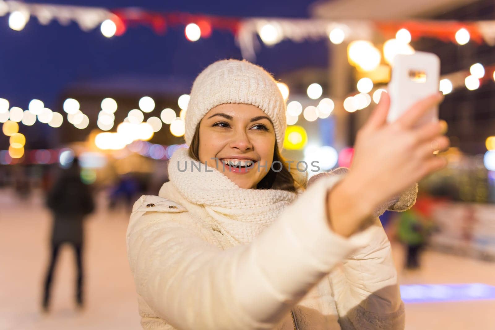 Happy young woman in winter on the ice rink taking picture on smartphone.