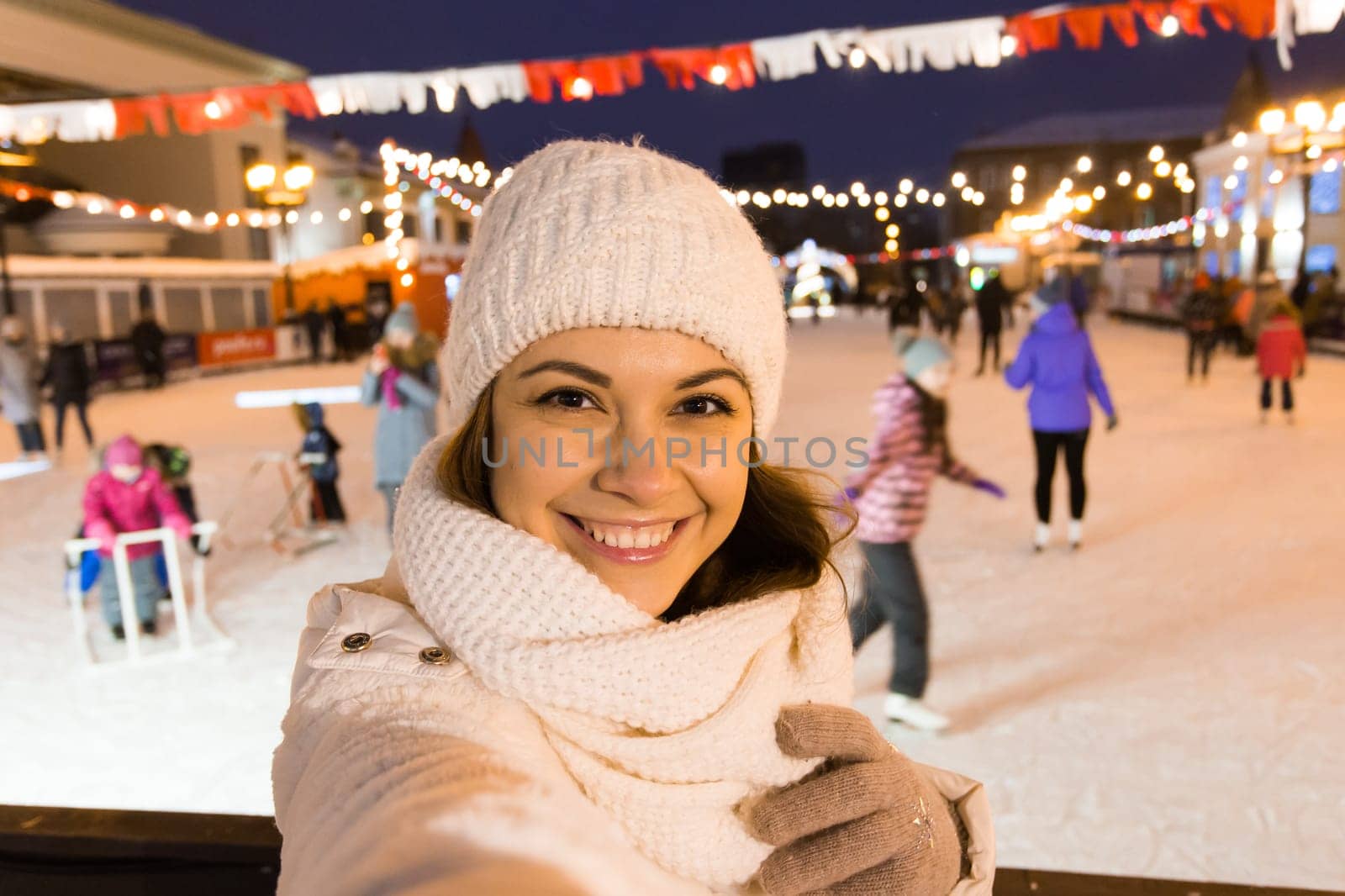 Christmas, winter, technology and leisure concept - happy young woman taking picture with smartphone on ice skating rink.
