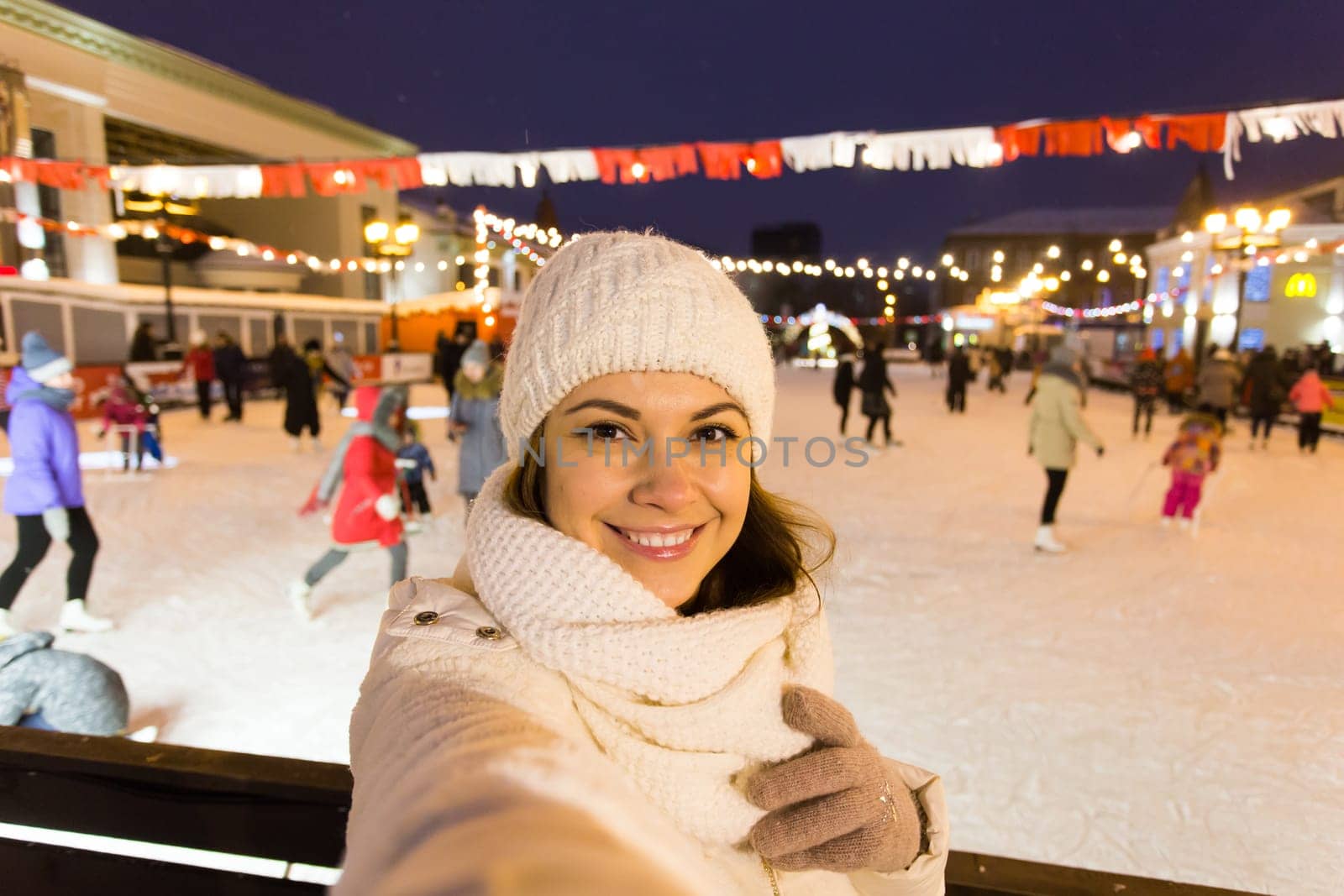 Happy young woman in winter on the ice rink taking picture on smartphone.