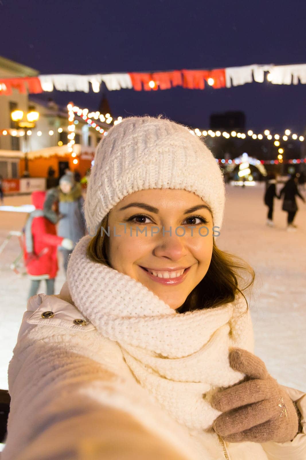 Christmas, winter, technology and leisure concept - happy young woman taking picture with smartphone on ice skating rink.