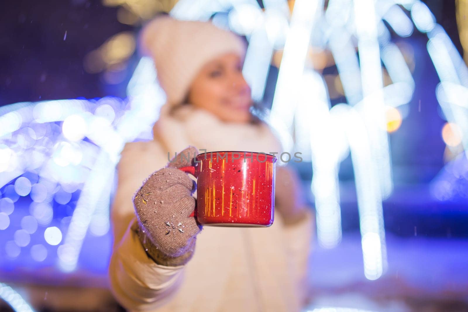 Girl standing over winter christmas city background snow snow drifts, stands warm jacket hat, holds cup tea with tea drinks.