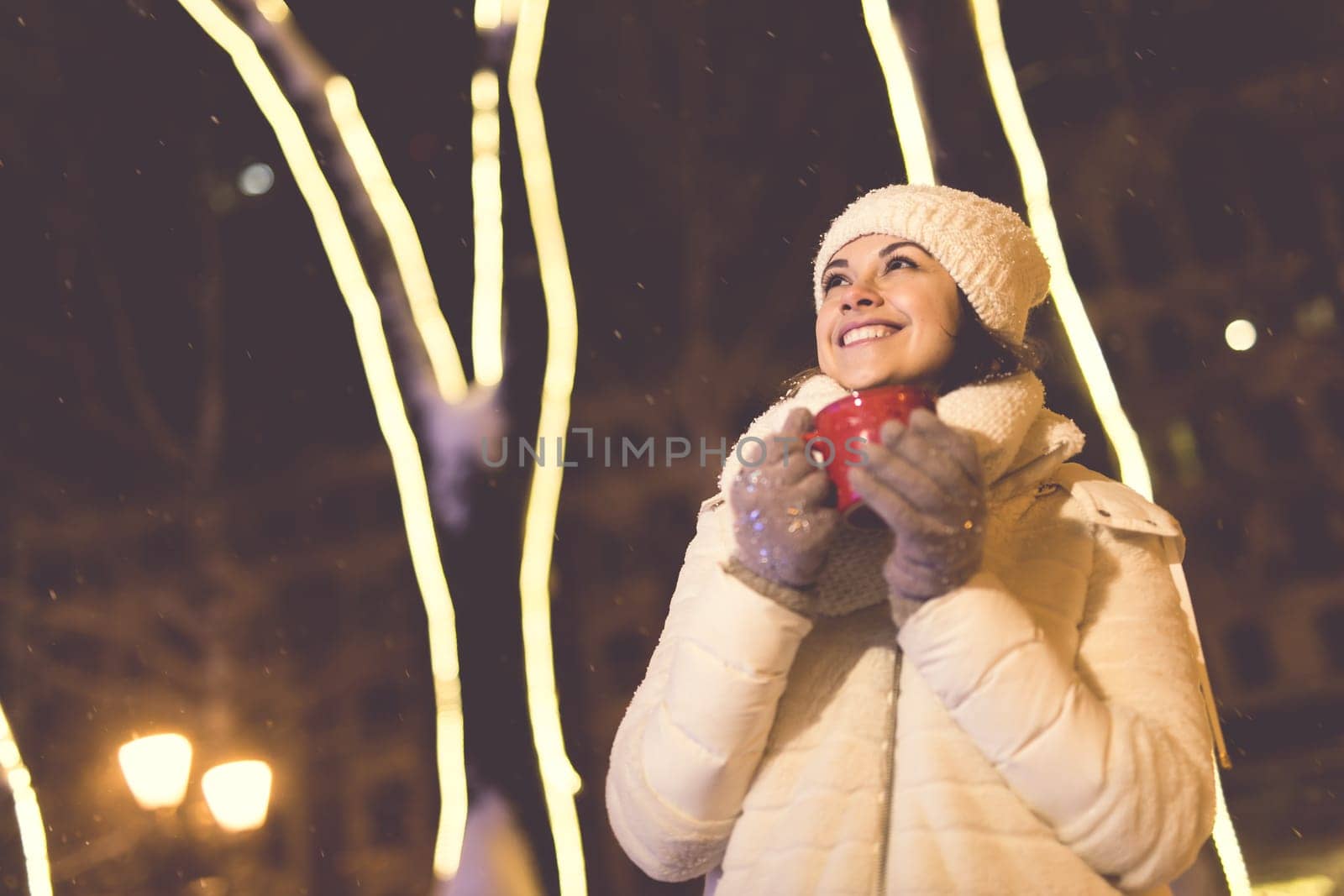 Christmas holidays. Beautiful smiling woman in warm clothing with cup of hot coffee outdoor in winter