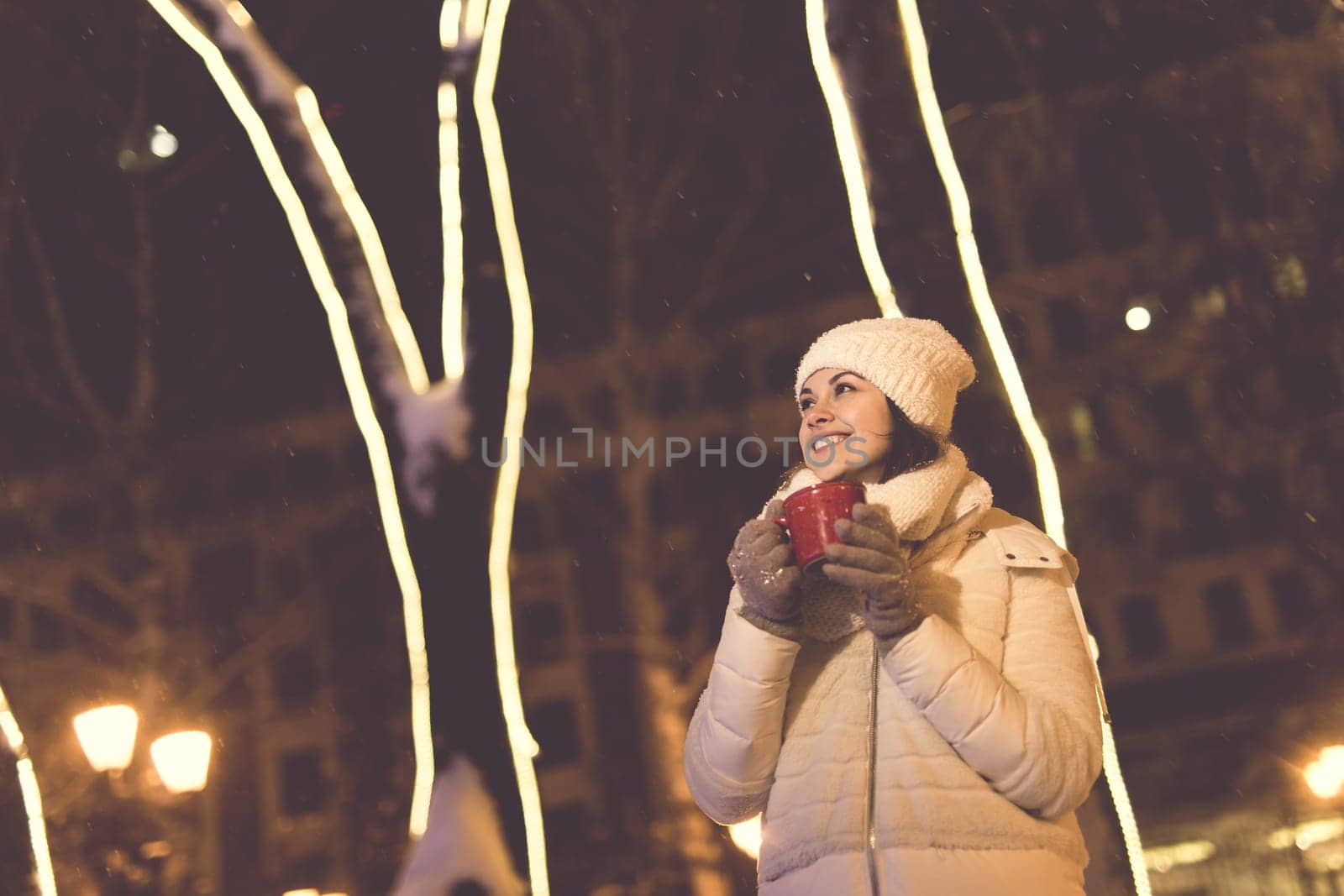 Christmas holidays. Beautiful smiling woman in warm clothing with cup of hot coffee outdoor in winter