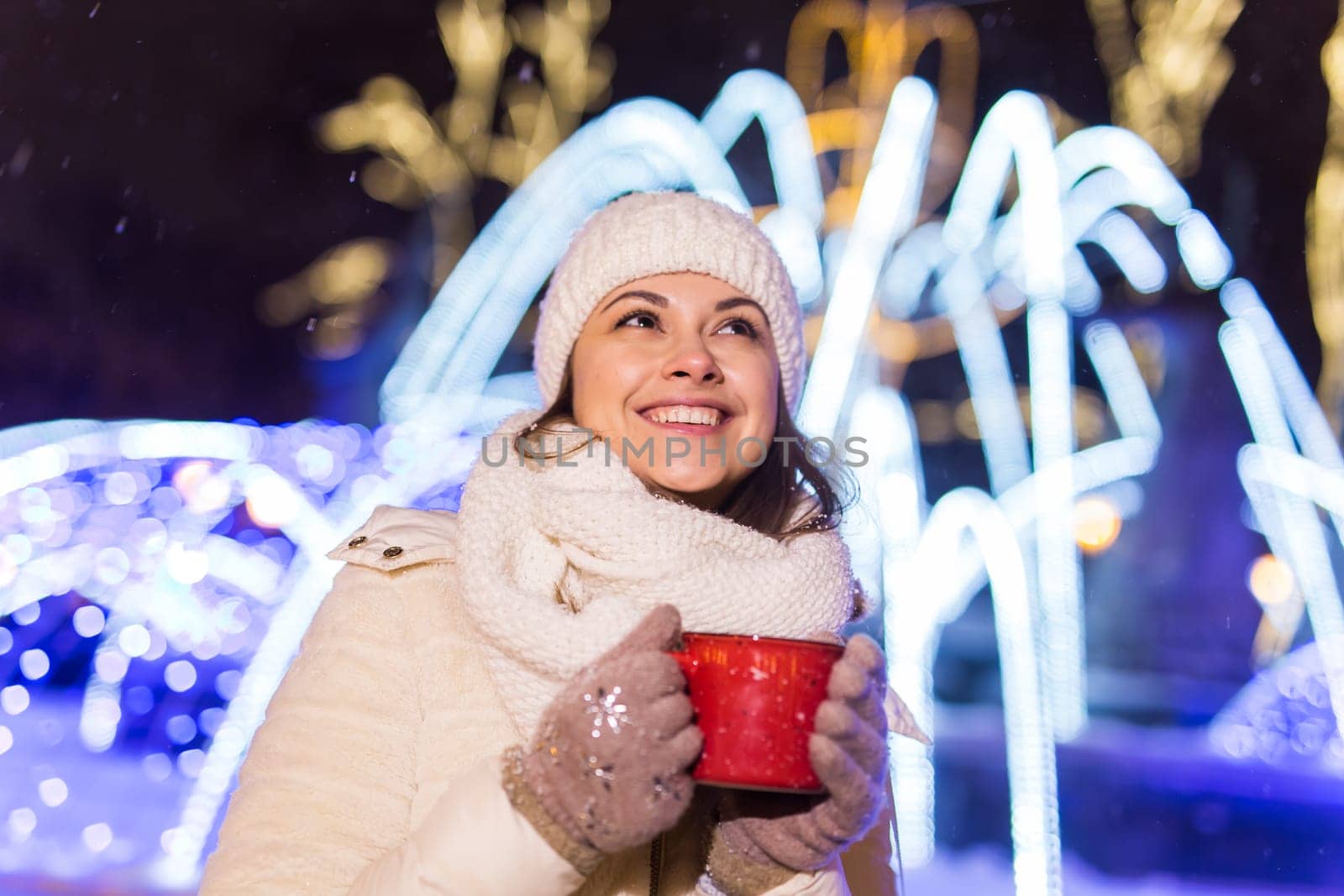 Christmas holidays. Beautiful smiling woman in warm clothing with cup of hot coffee outdoor in winter