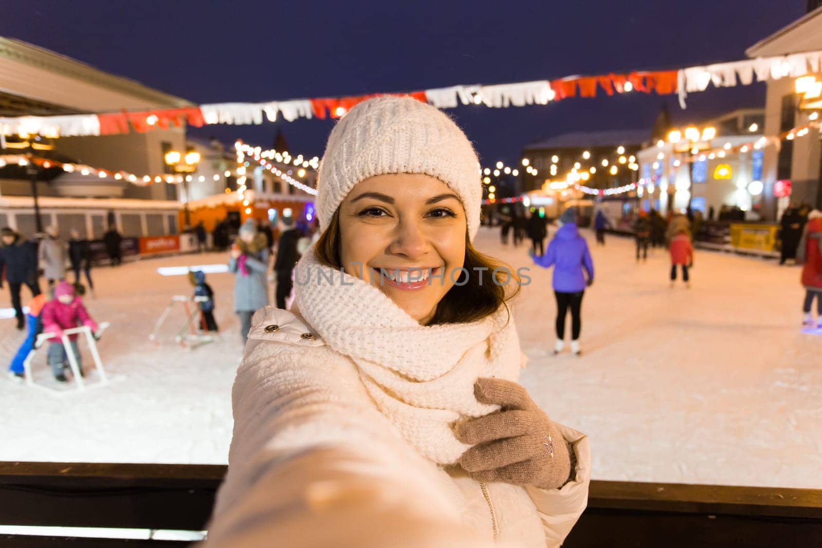 Happy young woman in winter on the ice rink taking picture on smartphone.