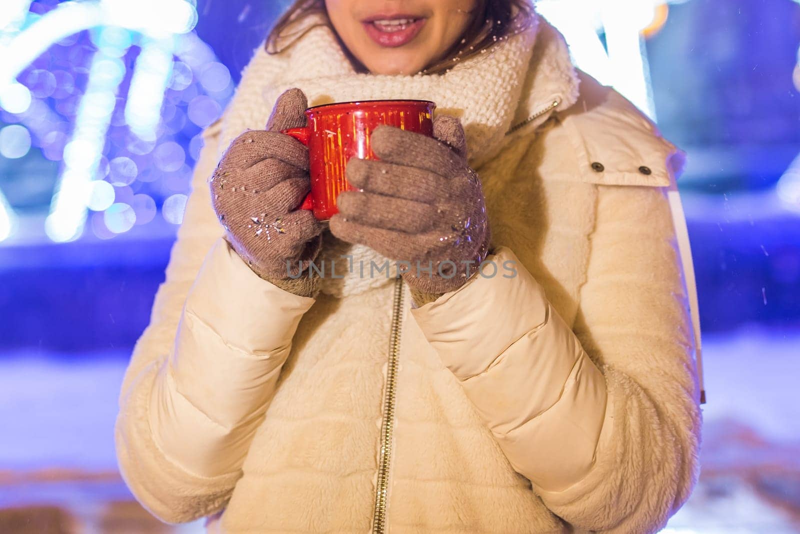 Girl standing over winter christmas city background snow snow drifts, stands warm jacket hat, holds cup tea with tea drinks.
