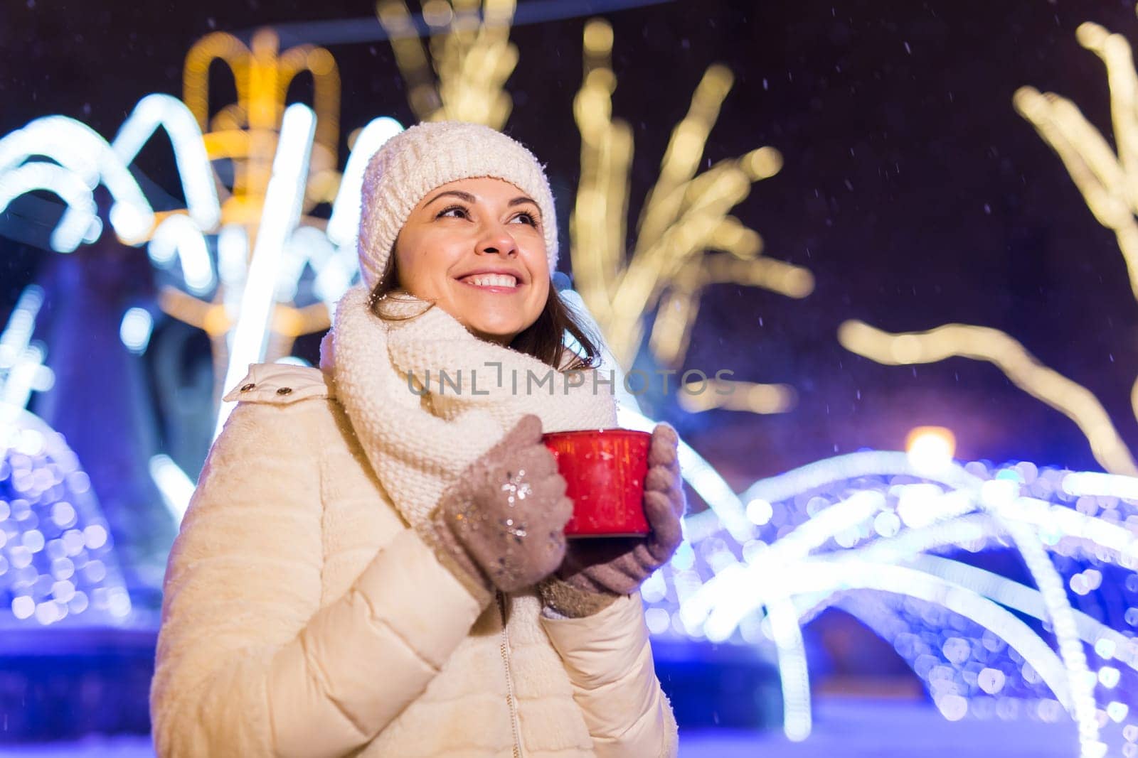 Christmas holidays. Beautiful smiling woman in warm clothing with cup of hot coffee outdoor in winter