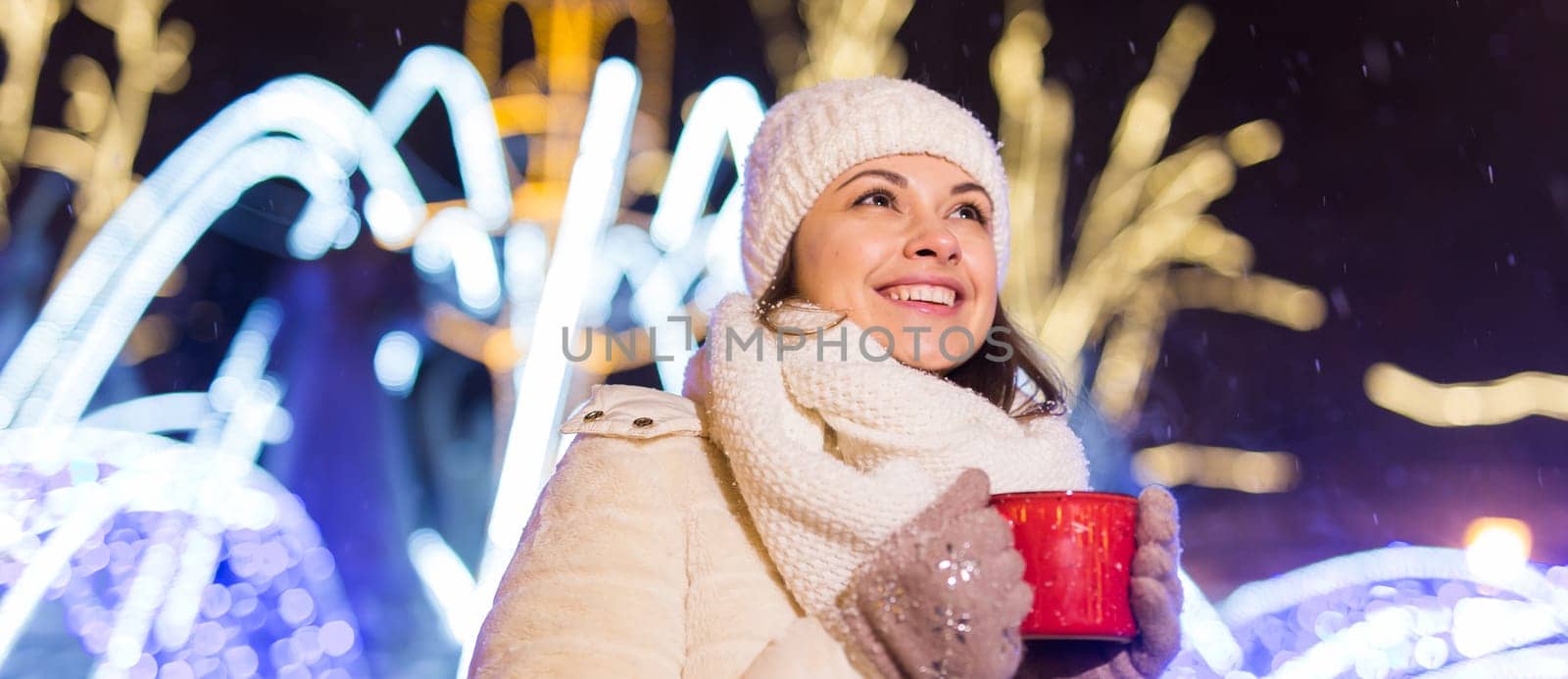 Christmas holidays. Beautiful smiling woman in warm clothing with cup of hot coffee outdoor in winter