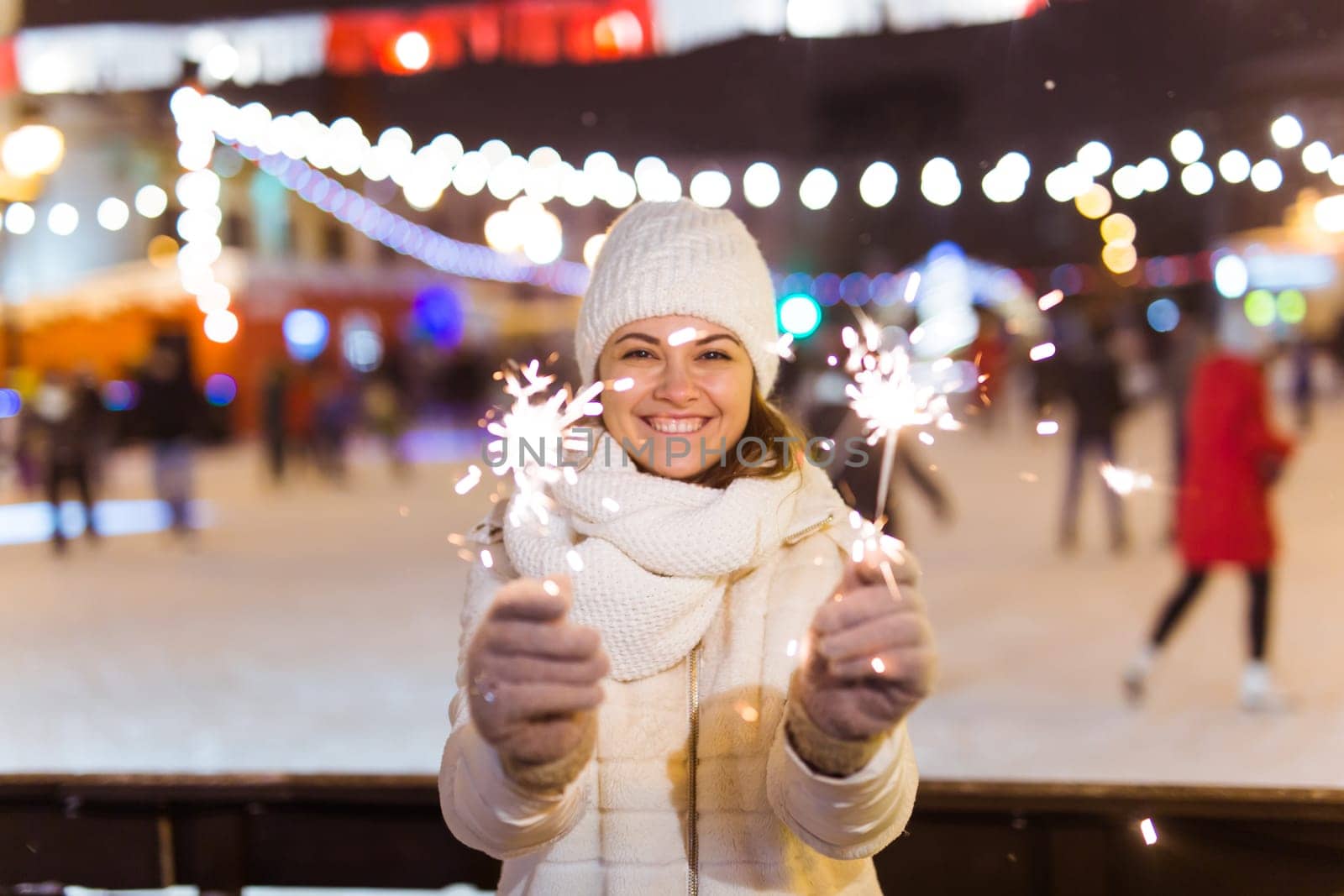Girl holding a sparkler in her hand. Outdoor winter city background, snow, snowflakes
