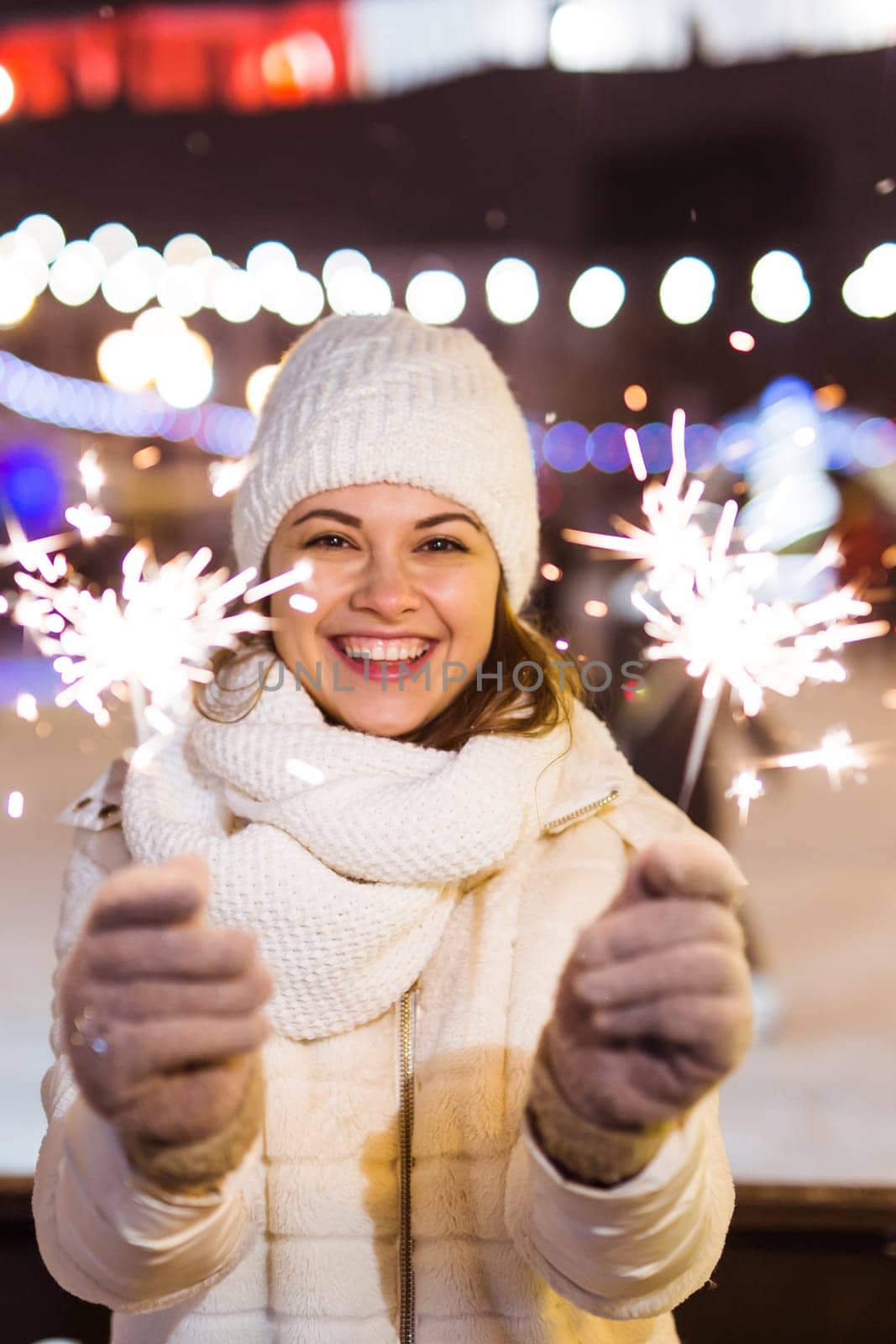 young woman wearing winter knitted clothes holding sparkler outdoors over snow background. Christmas holidays.