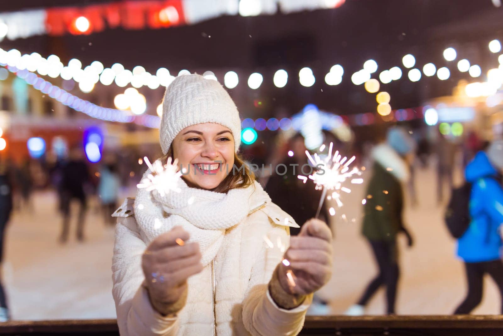 Girl holding a sparkler in her hand. Outdoor winter city background, snow, snowflakes