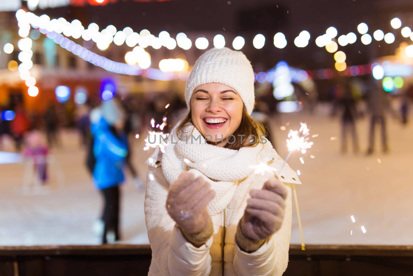 young woman wearing winter knitted clothes holding sparkler outdoors over snow background. Christmas holidays.