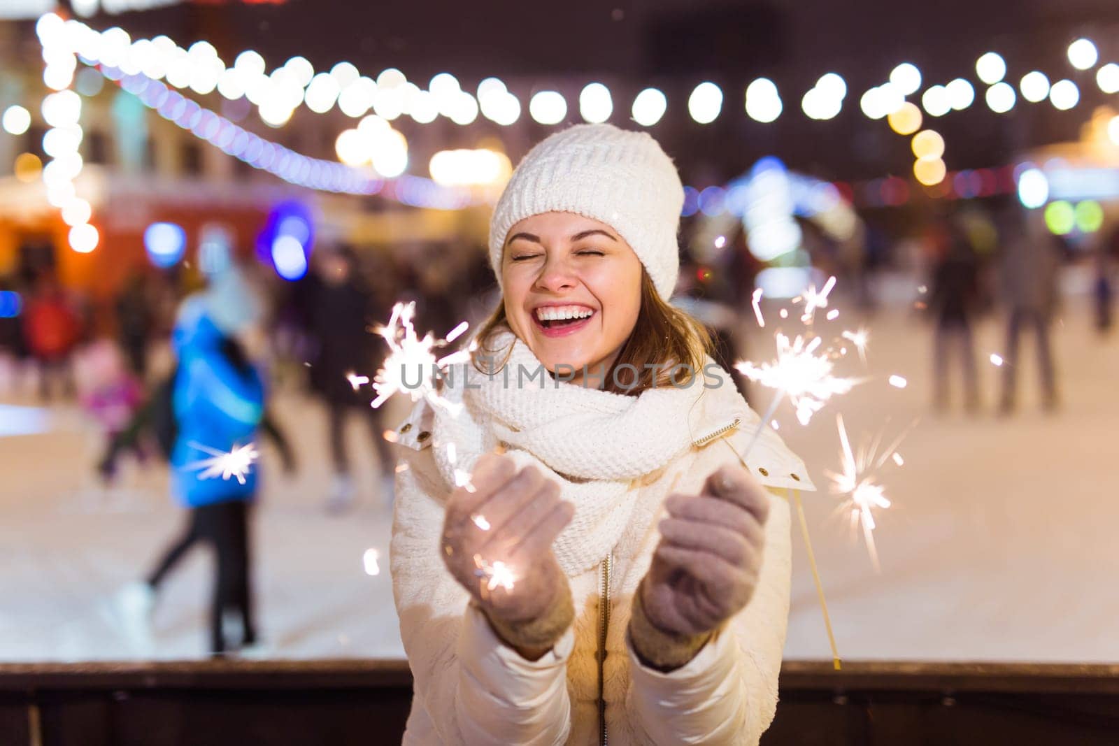 Young beautiful woman in knitted hat and scarf standing in the city with bengal light, sparkler. Concept celebration and christmas
