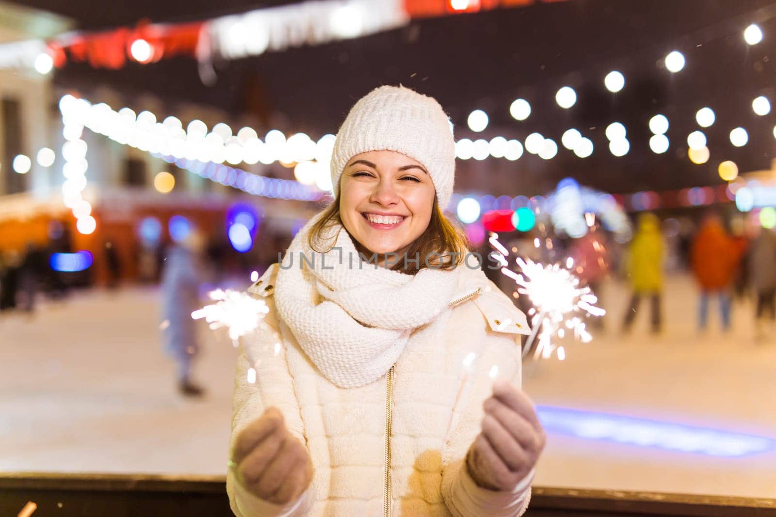 young woman wearing winter knitted clothes holding sparkler outdoors over snow background. Christmas holidays.