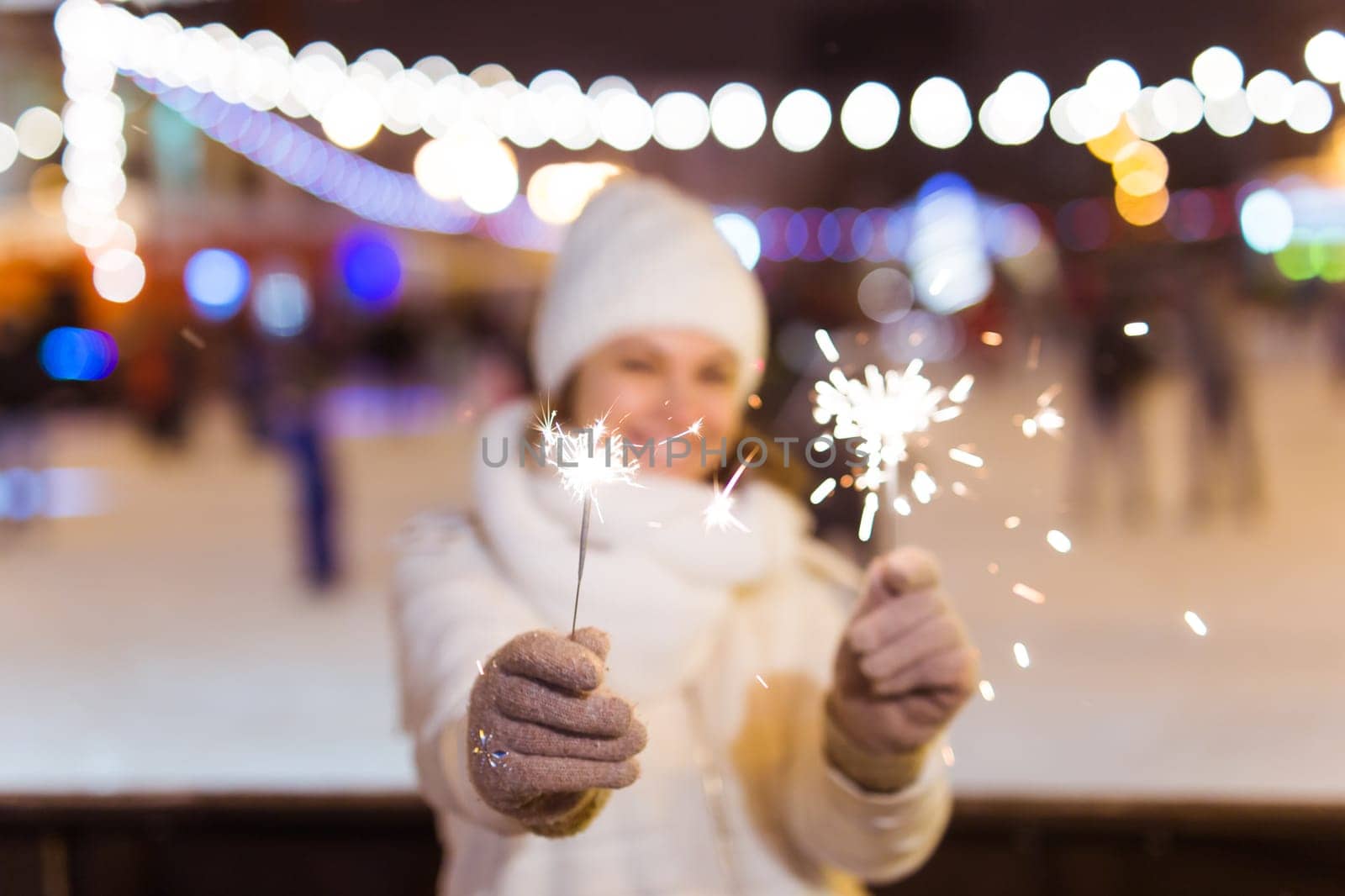 Young beautiful woman in knitted hat and scarf standing in the city with bengal light, sparkler. Concept celebration and christmas