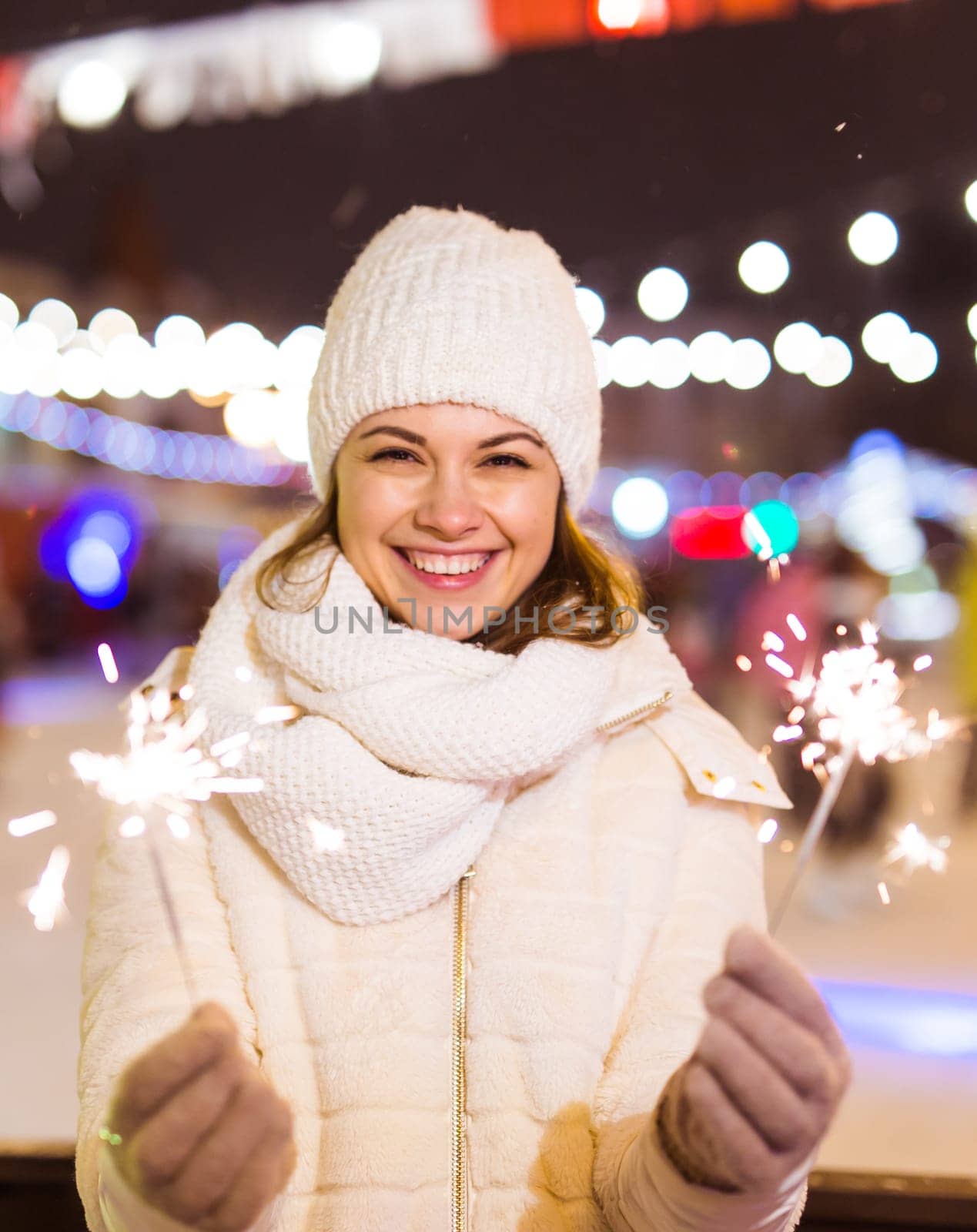 Young beautiful woman in knitted hat and scarf standing in the city with bengal light, sparkler. Concept celebration and christmas