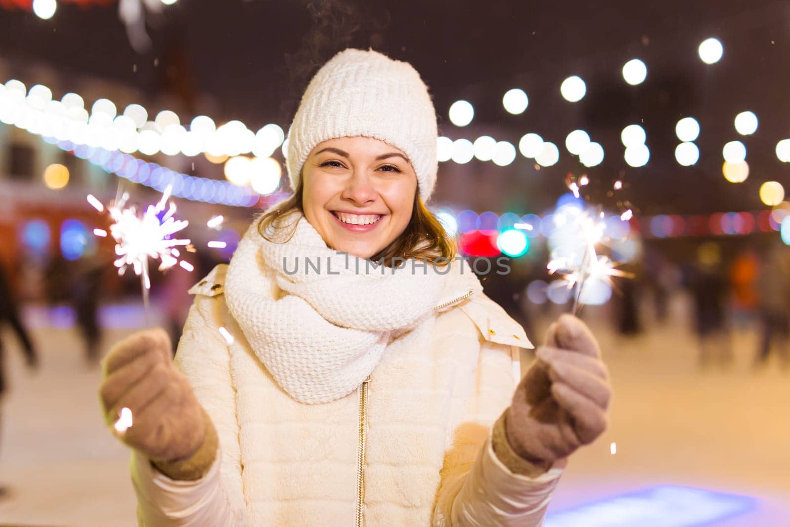 Young beautiful woman in knitted hat and scarf standing in the city with bengal light, sparkler. Concept celebration and christmas