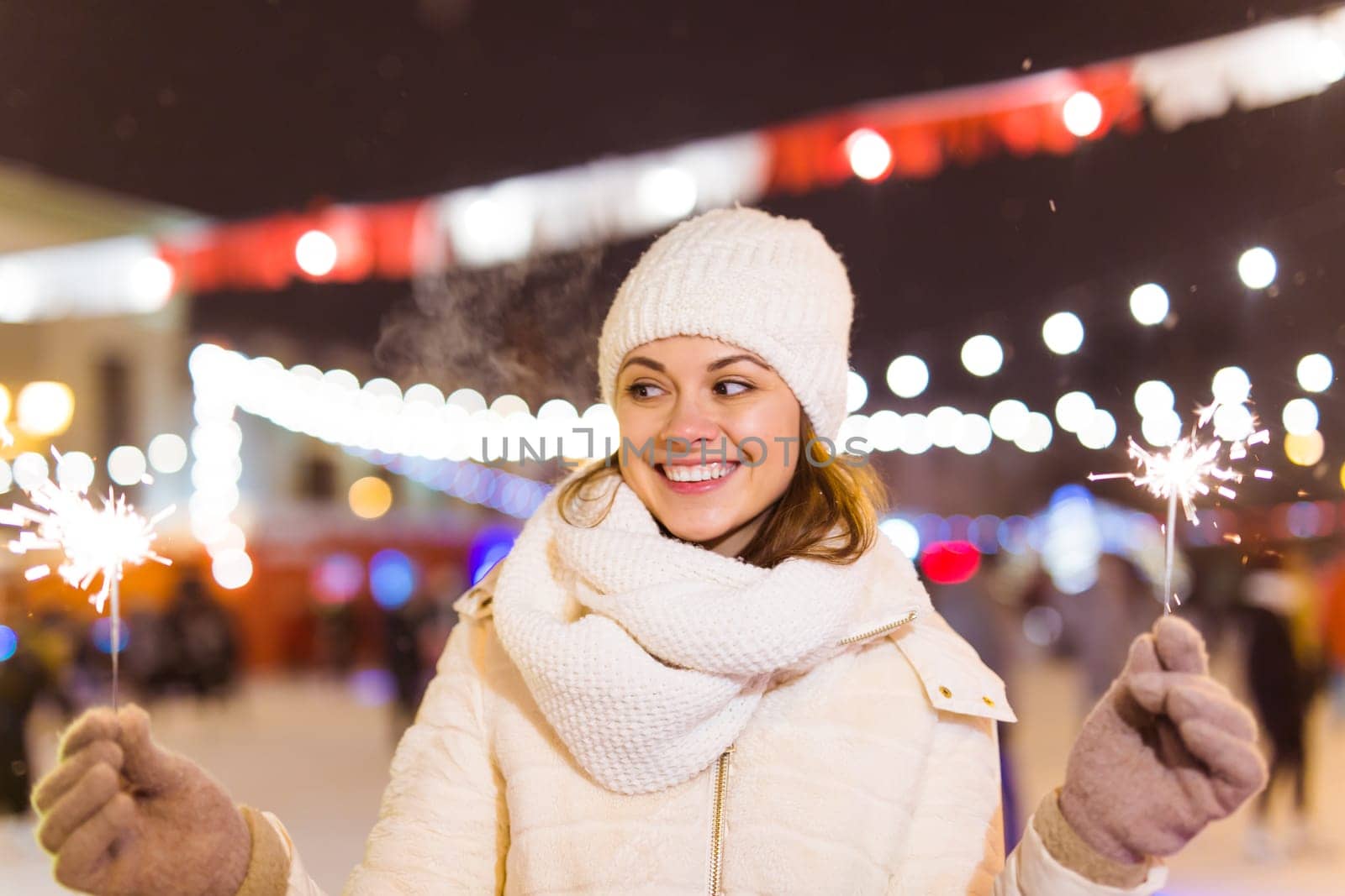Girl holding a sparkler in her hand. Outdoor winter city background, snow, snowflakes