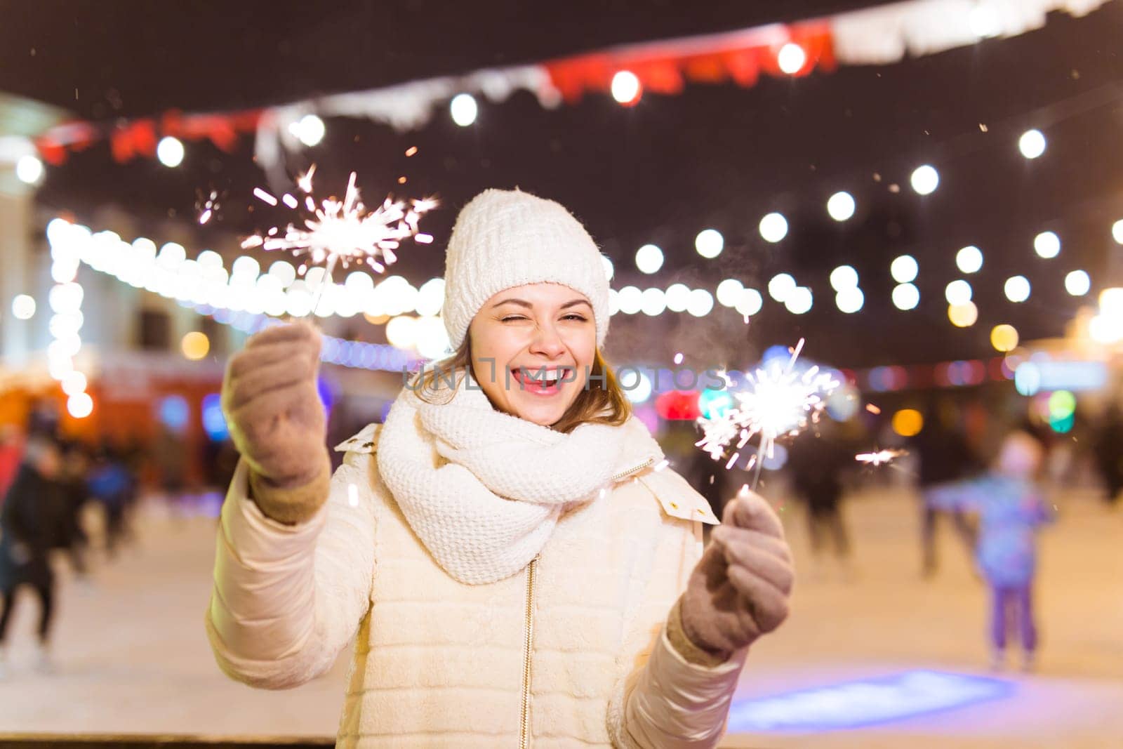 Girl holding a sparkler in her hand. Outdoor winter city background, snow, snowflakes