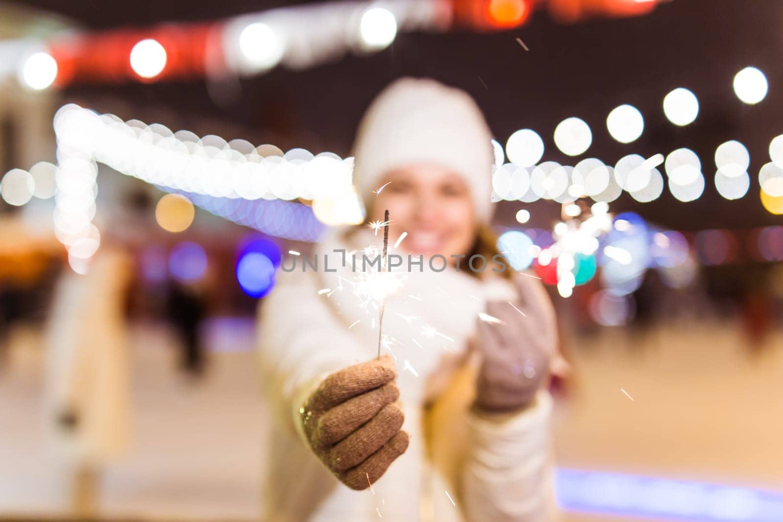 Young beautiful woman in knitted hat and scarf standing in the city with bengal light, sparkler. Concept celebration and christmas