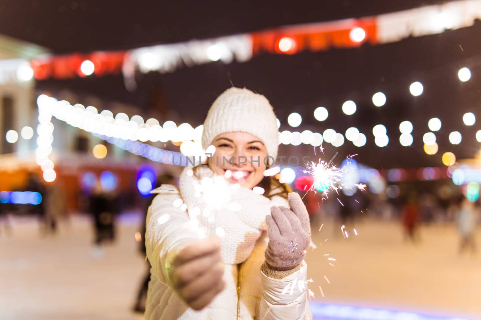 Girl holding a sparkler in her hand. Outdoor winter city background, snow, snowflakes