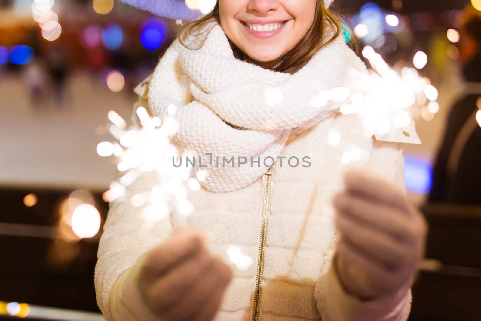 young woman wearing winter knitted clothes holding sparkler outdoors over snow background. Christmas holidays.
