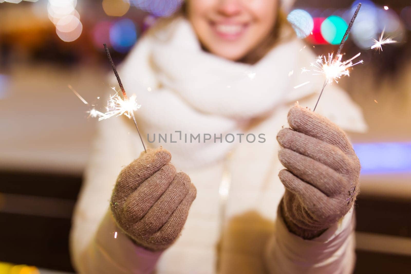 young woman wearing winter knitted clothes holding sparkler outdoors over snow background. Christmas holidays.