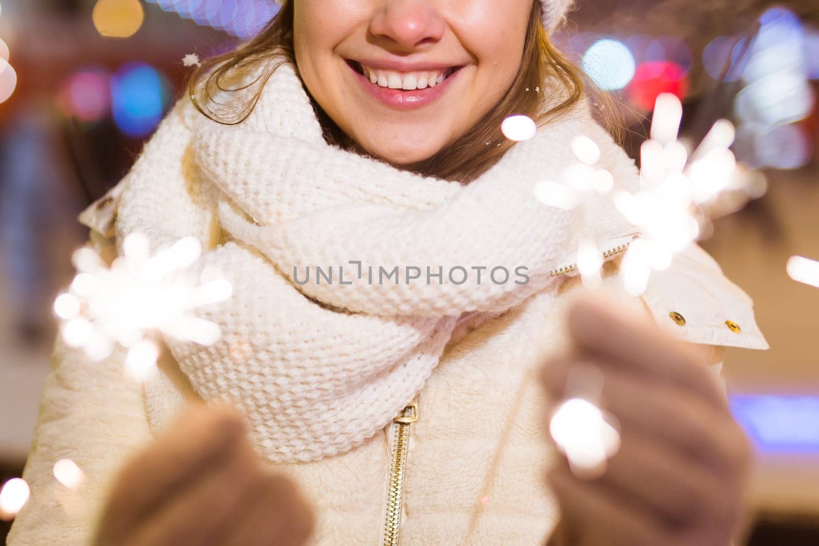 Young beautiful woman in knitted hat and scarf standing in the city with bengal light, sparkler. Concept celebration and christmas