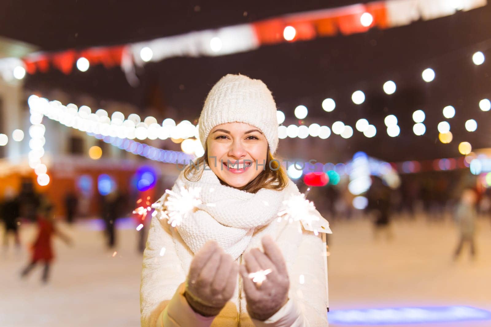 Girl holding a sparkler in her hand. Outdoor winter city background, snow, snowflakes