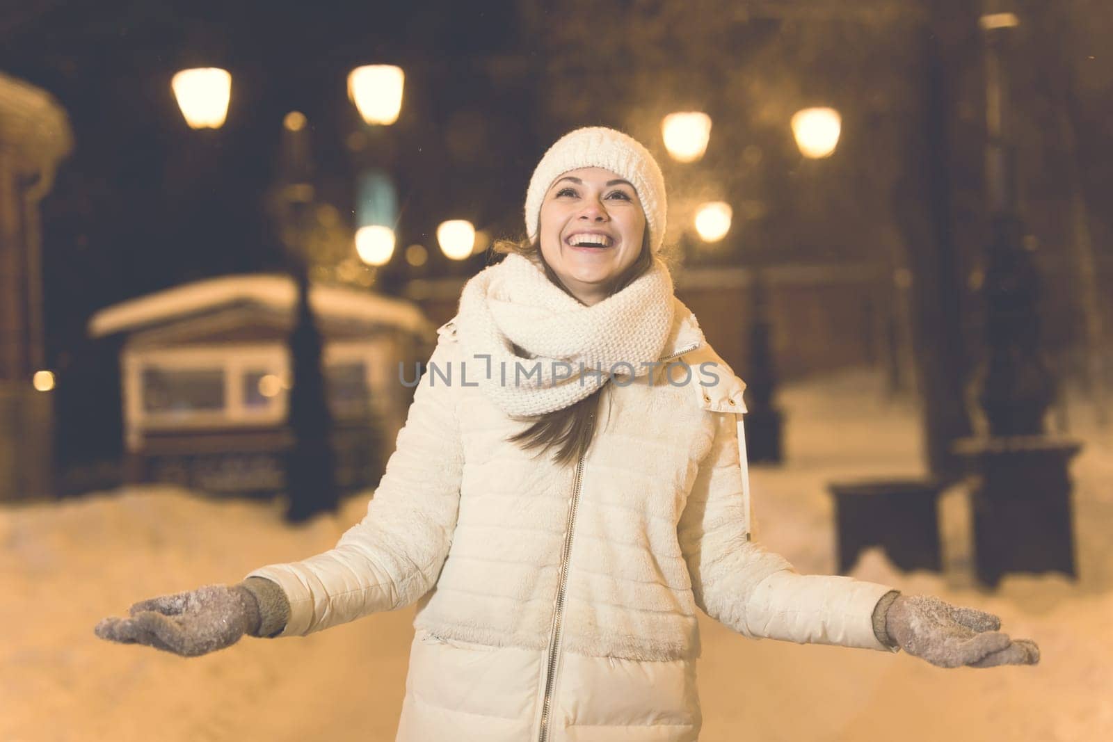 Girl having fun christmas decoration lights street. Young happy smiling woman wearing stylish knitted scarf and jacket outdoors. Model laughing. Winter wonderland city scene, New Year party.