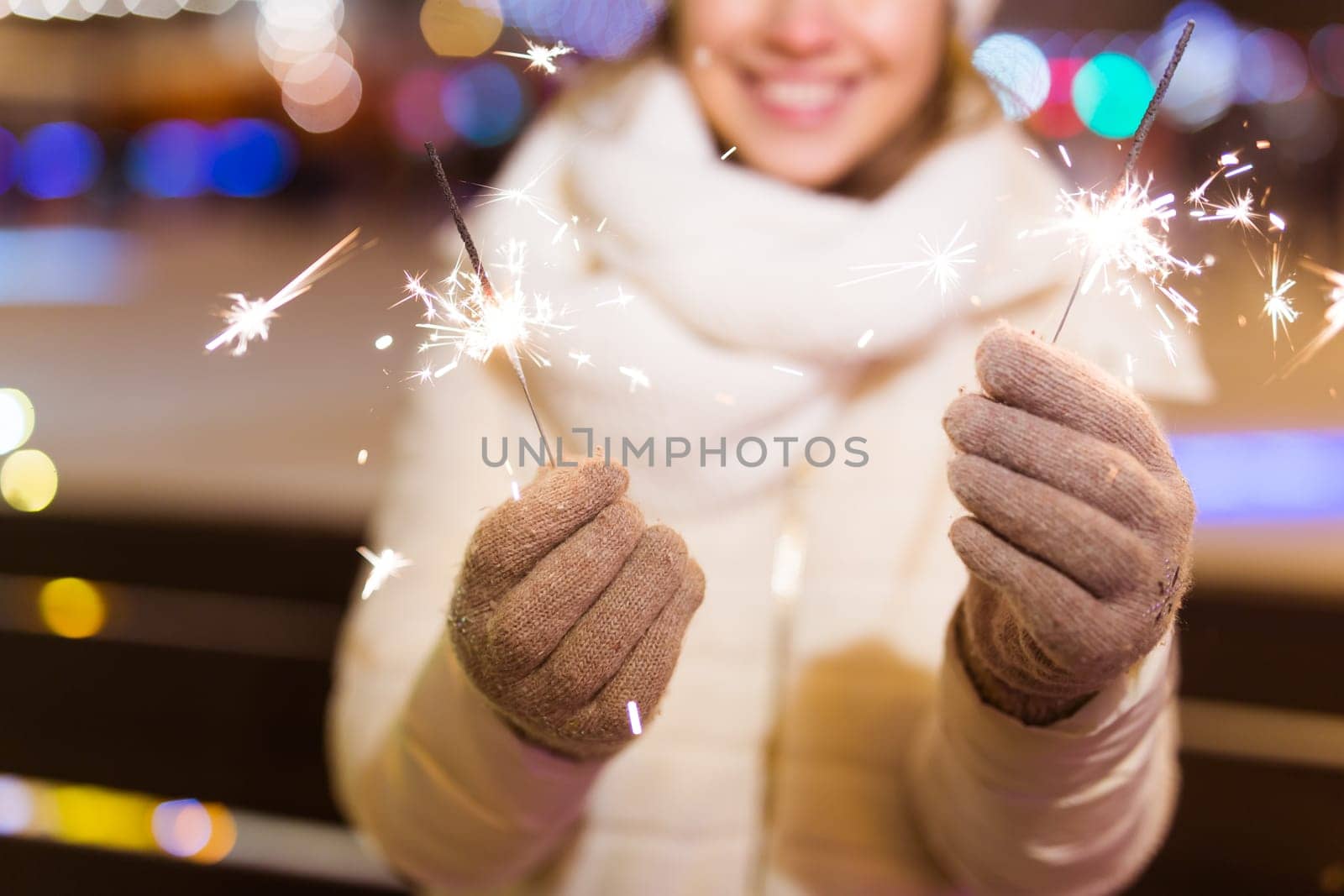Girl holding a sparkler in her hand. Outdoor winter city background, snow, snowflakes