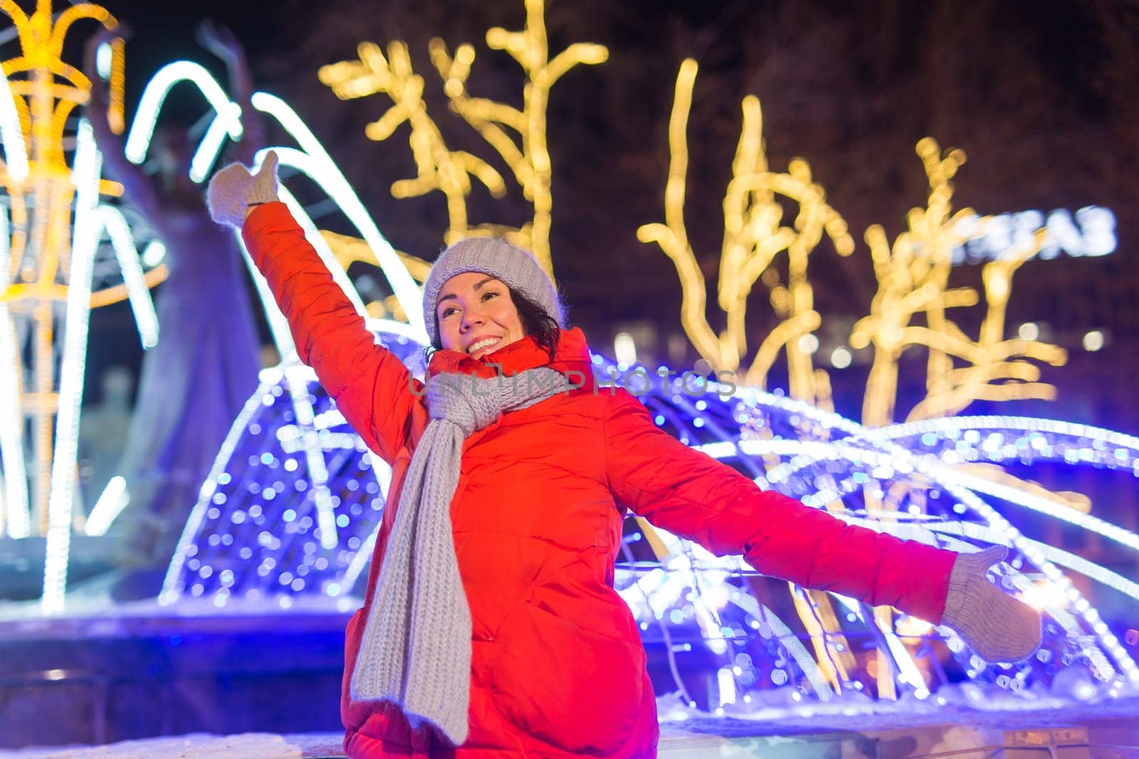Girl having fun christmas decoration lights street. Young happy smiling woman wearing stylish knitted scarf and jacket outdoors. Model laughing. Winter wonderland city scene, New Year party.